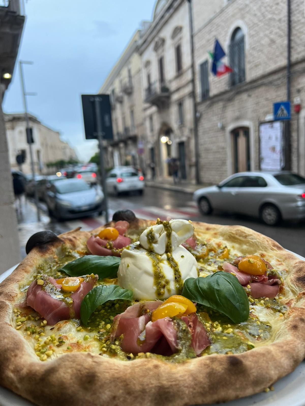Una pizza con molti condimenti è appoggiata su un piatto davanti a un edificio.
