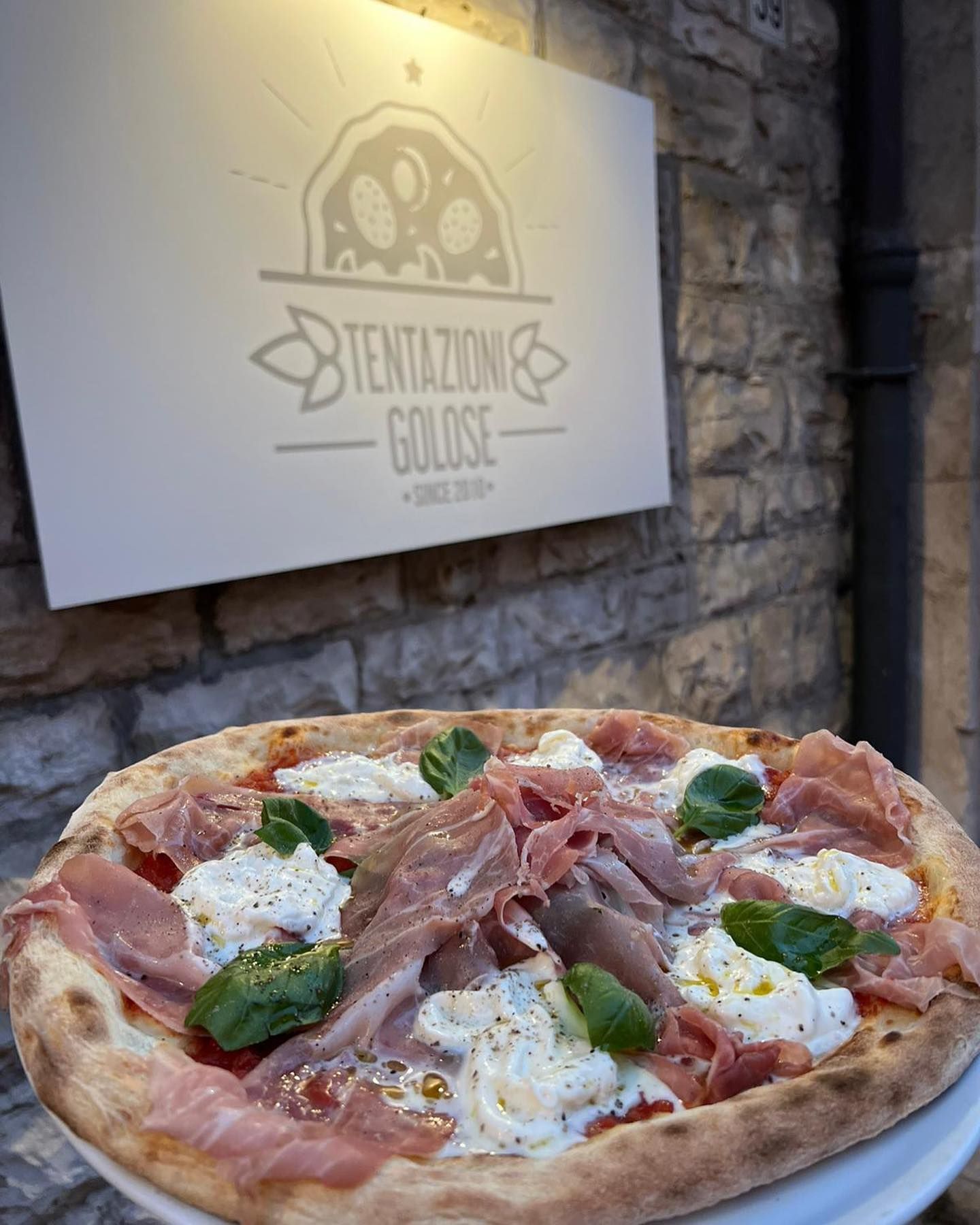 Una pizza è appoggiata su un piatto davanti a un cartello che dice tentazione golose