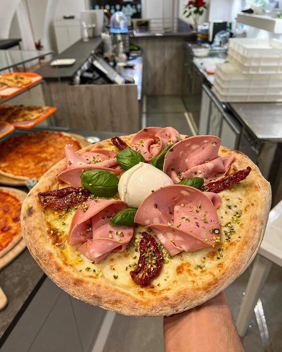 Una persona tiene in mano una pizza in cucina.