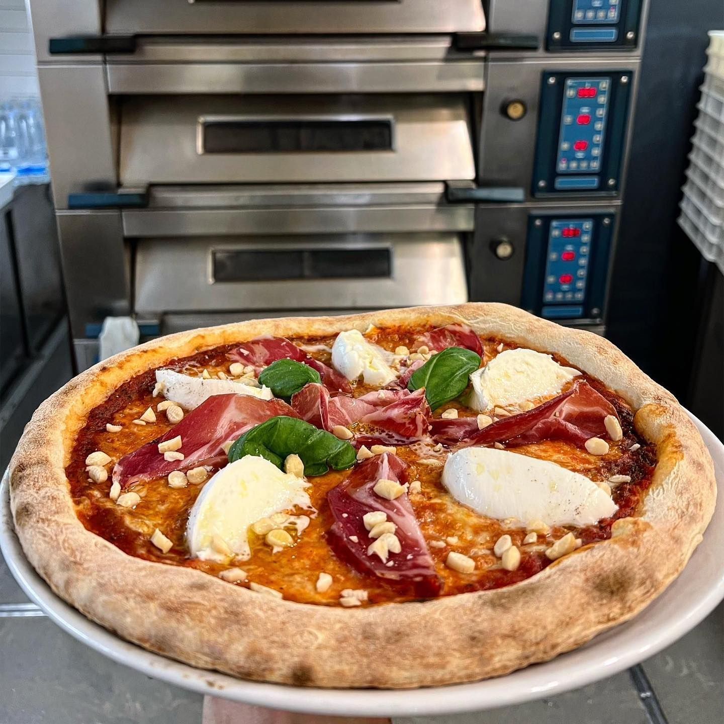 Una persona tiene in mano una pizza su un piatto davanti al forno.