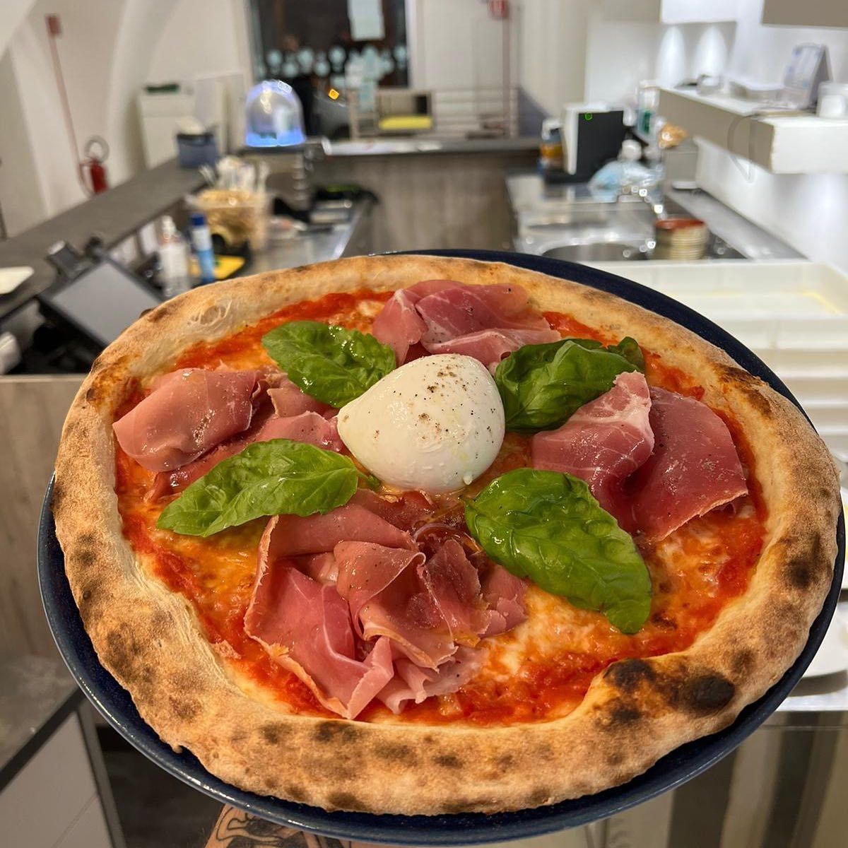 Una persona tiene in mano una pizza su un piatto in cucina.