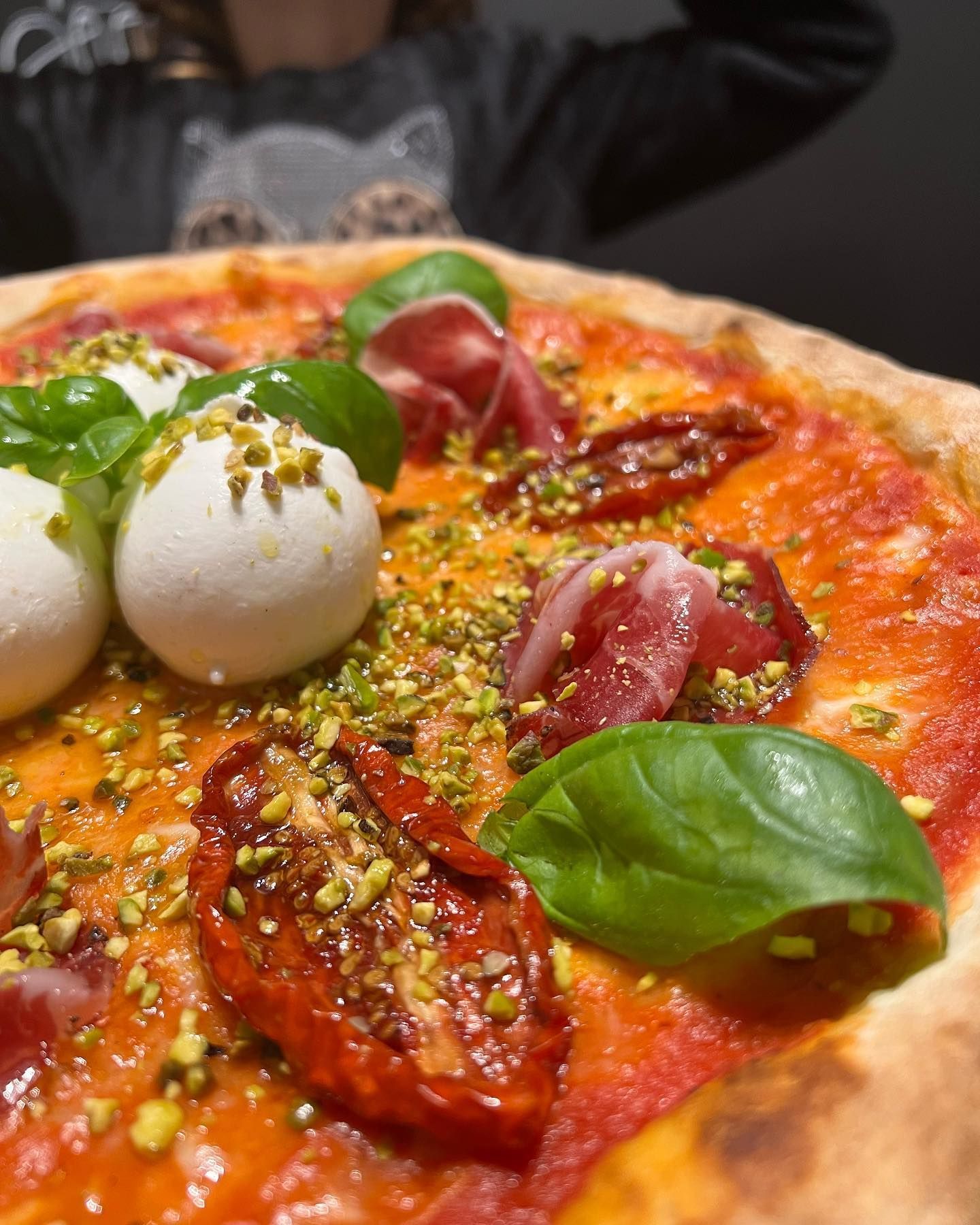 Un primo piano di una pizza con pomodori, mozzarella, basilico e pistacchi.