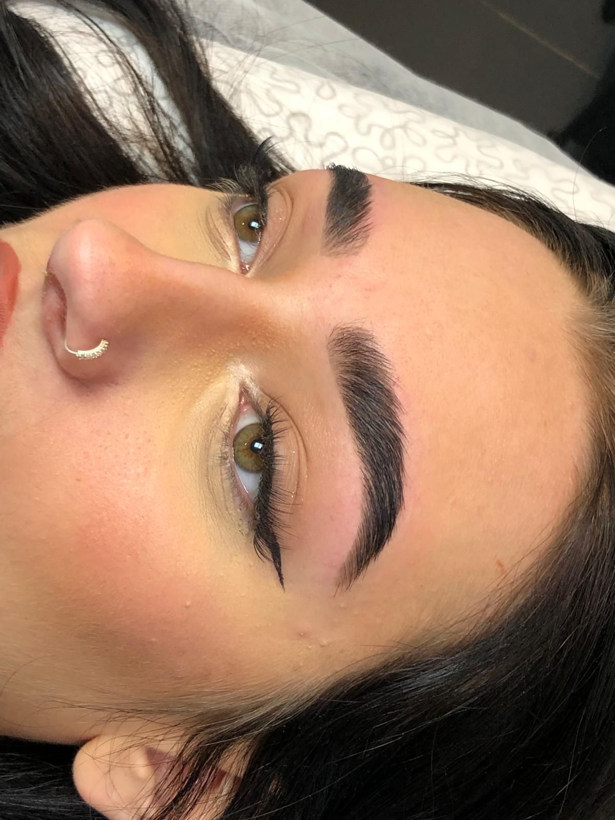 Persoon met donkere wenkbrauwen en eyeliner, liggend met open ogen.