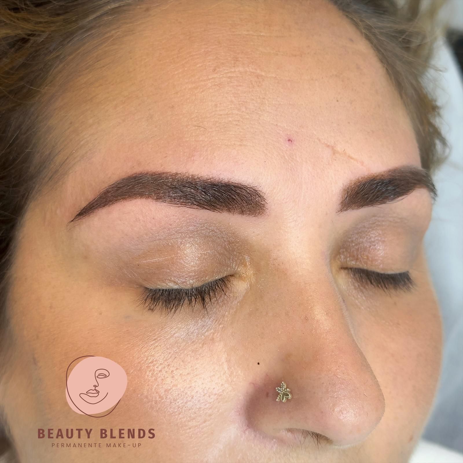 Vrouw met gesloten ogen, pas getatoeëerde donkerbruine wenkbrauwen en een neusring.