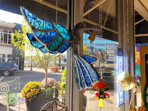 A stained glass hummingbird is hanging in a window.