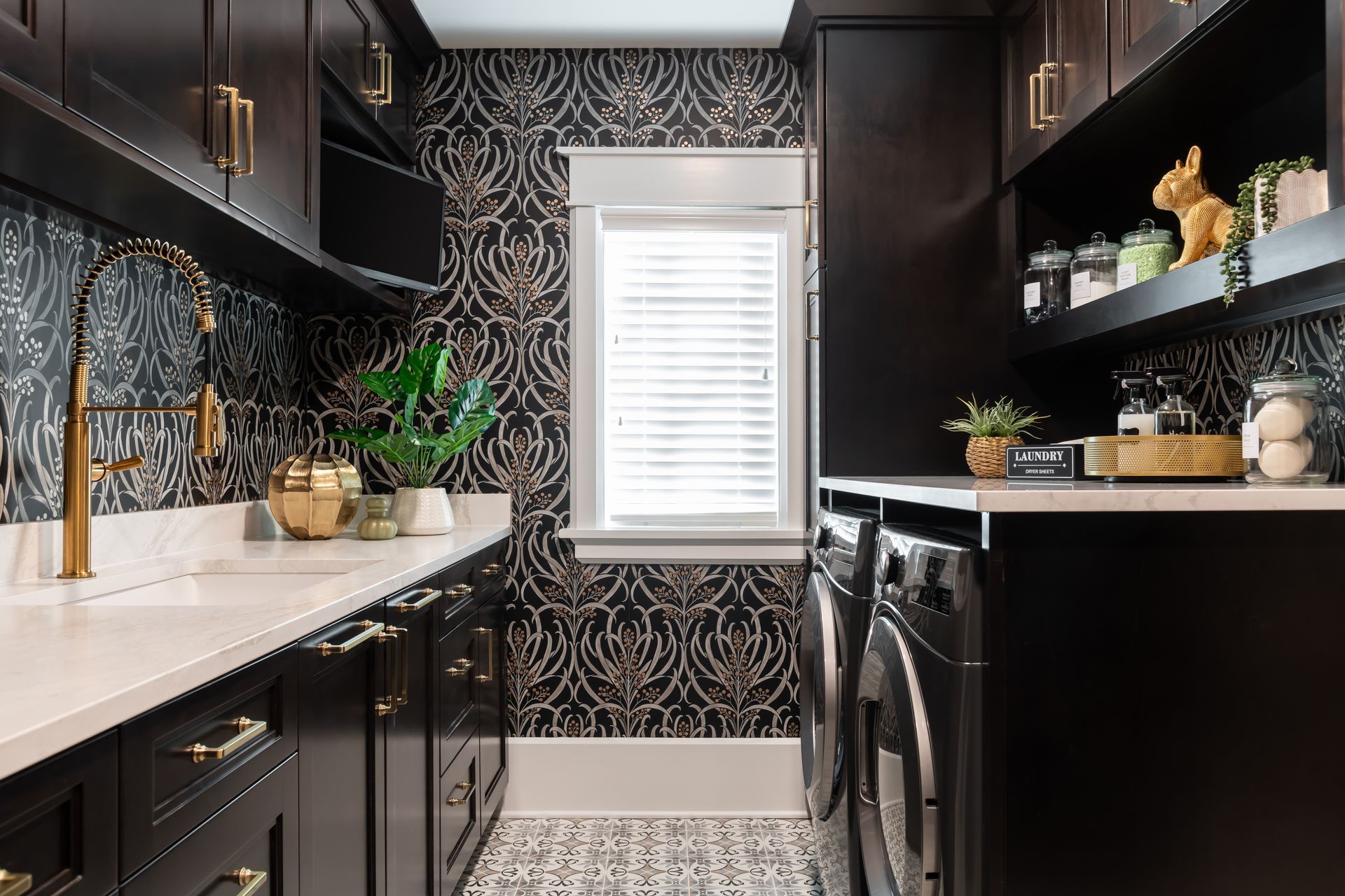 A laundry room with black cabinets , a washer and dryer , a sink , and a window.