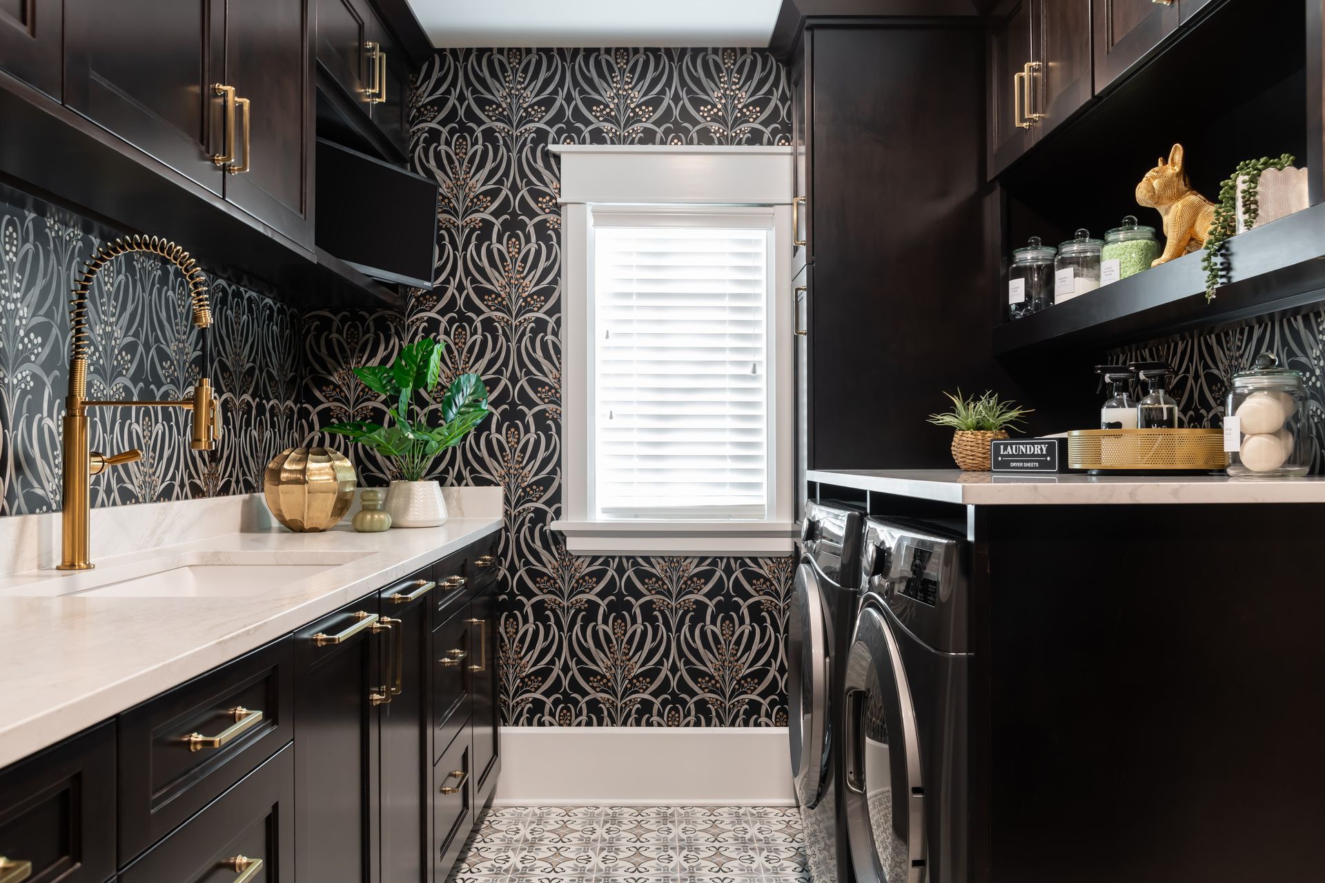 A laundry room with black cabinets , a washer and dryer , a sink , and a window.