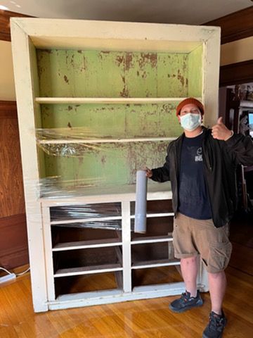 A man wearing a mask is standing in front of a large bookshelf.