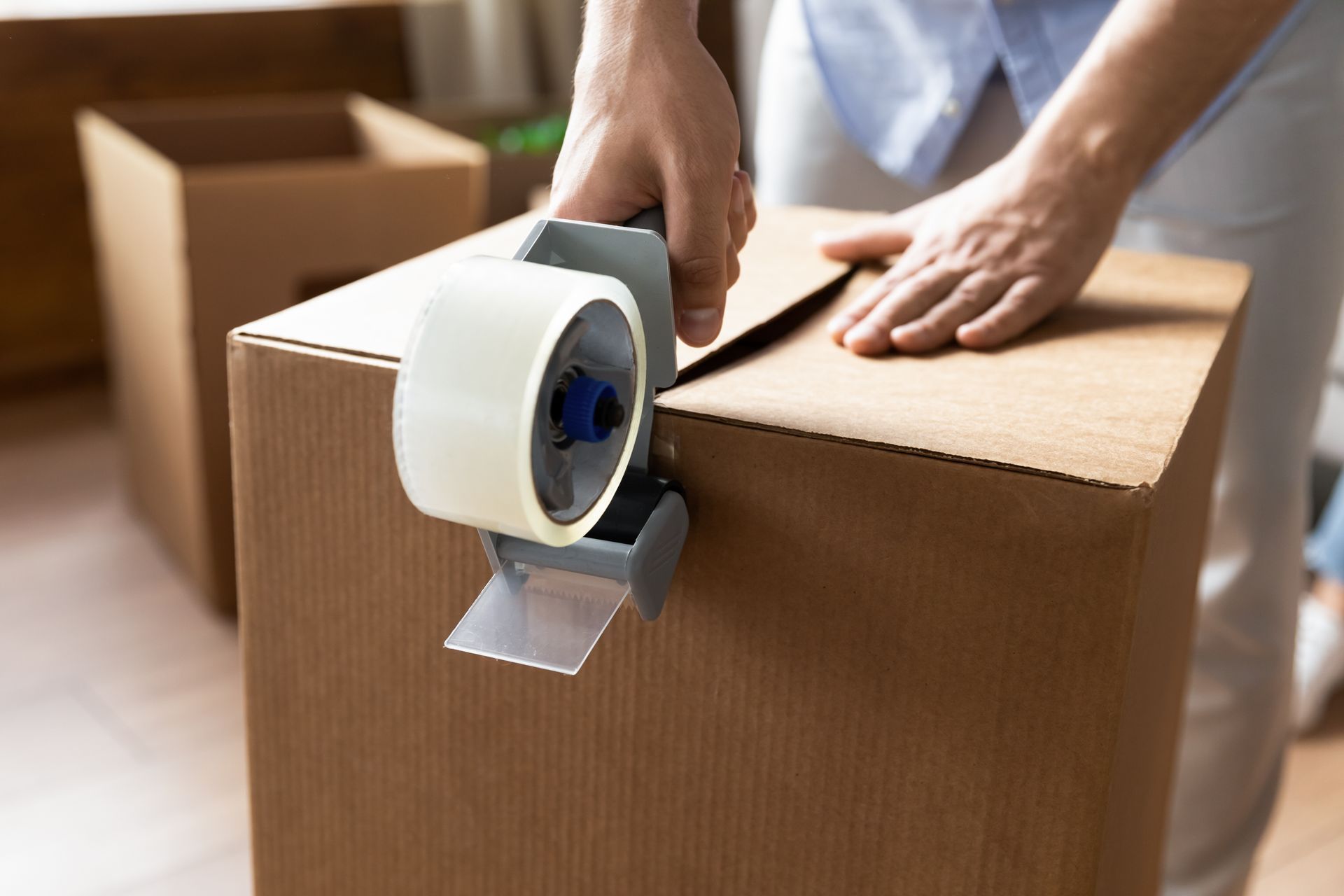Person sealing a cardboard box with packing tape, preparing for a move.