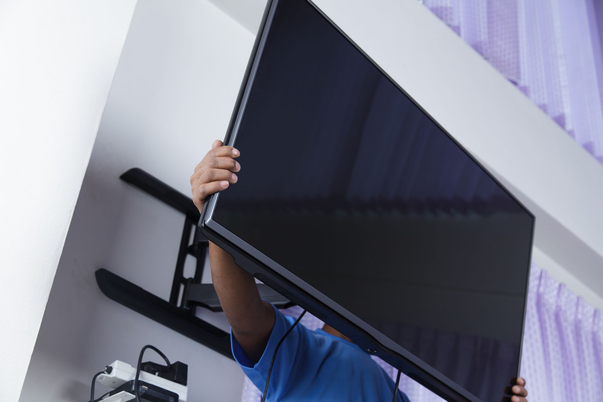 Person installs a large black TV on a wall mount.