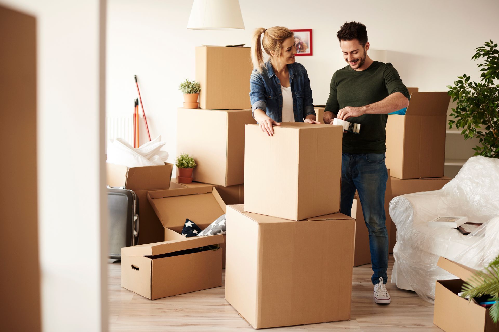 A couple packing moving boxes in a living room, smiling, surrounded by boxes, preparing to move.