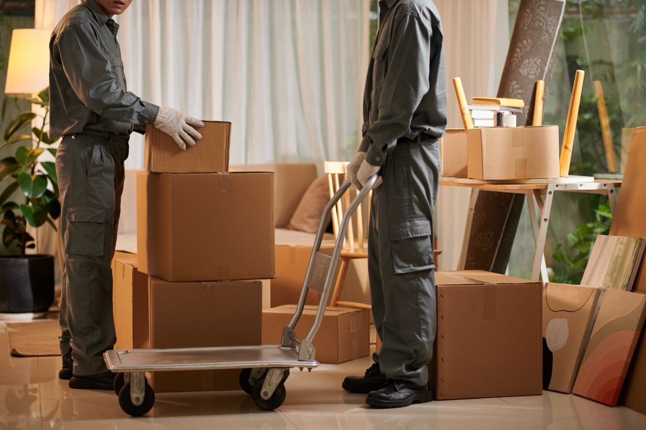 Two men are moving boxes on a dolly in a living room.
