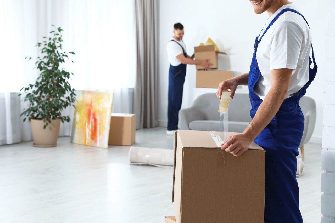 A man is wrapping a cardboard box with tape in a living room.
