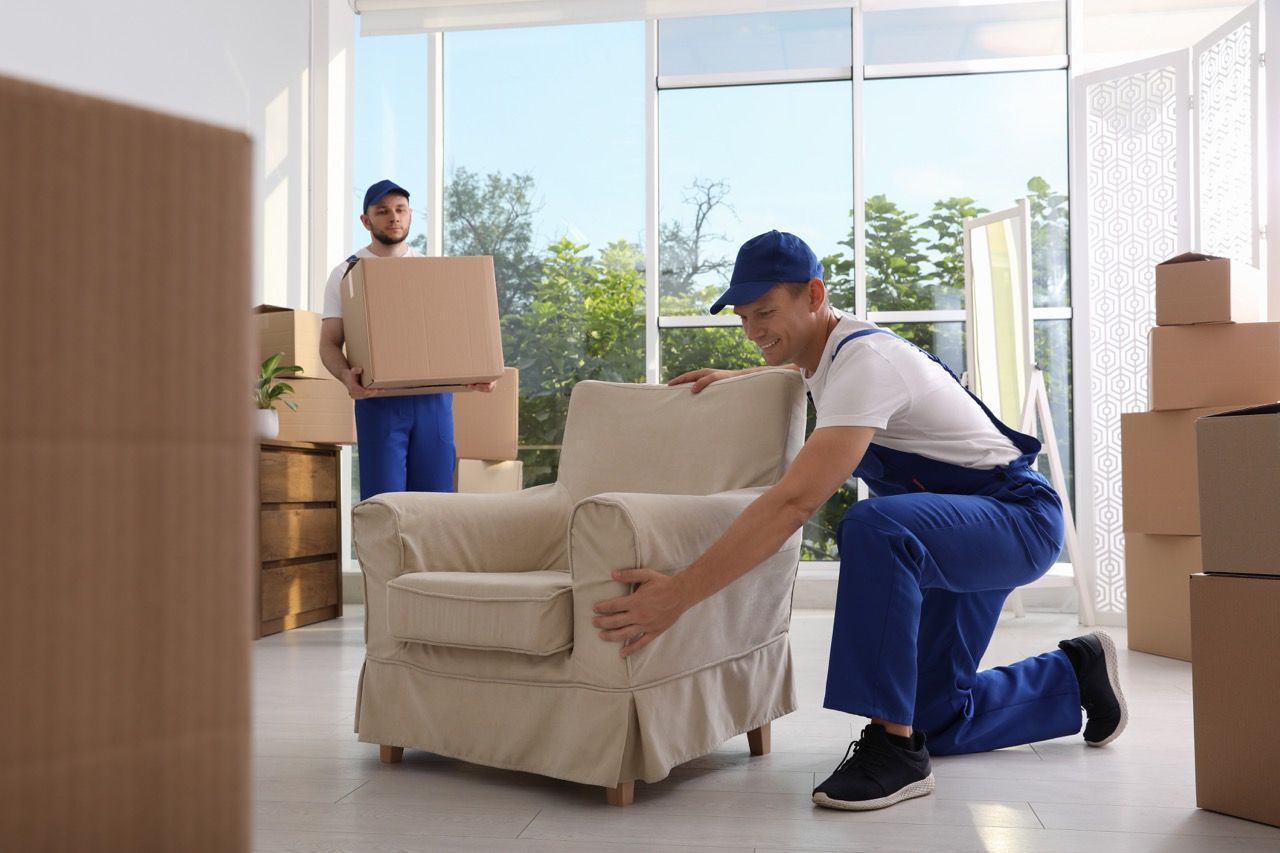 Two men are moving a chair in a living room.