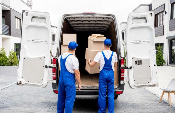 two men in blue overalls are loading boxes into a van