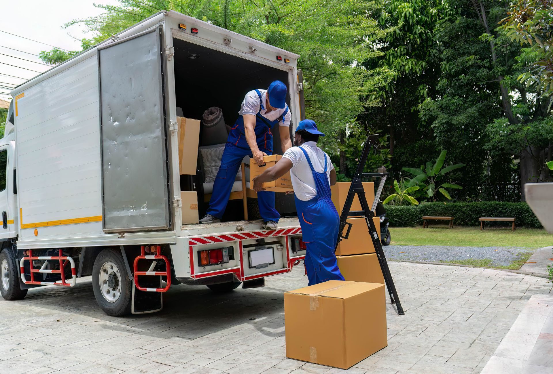 two men in blue overalls are loading boxes into a truck