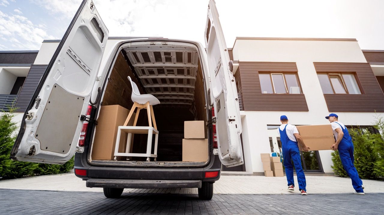 Two men are loading boxes into a van in front of a house.