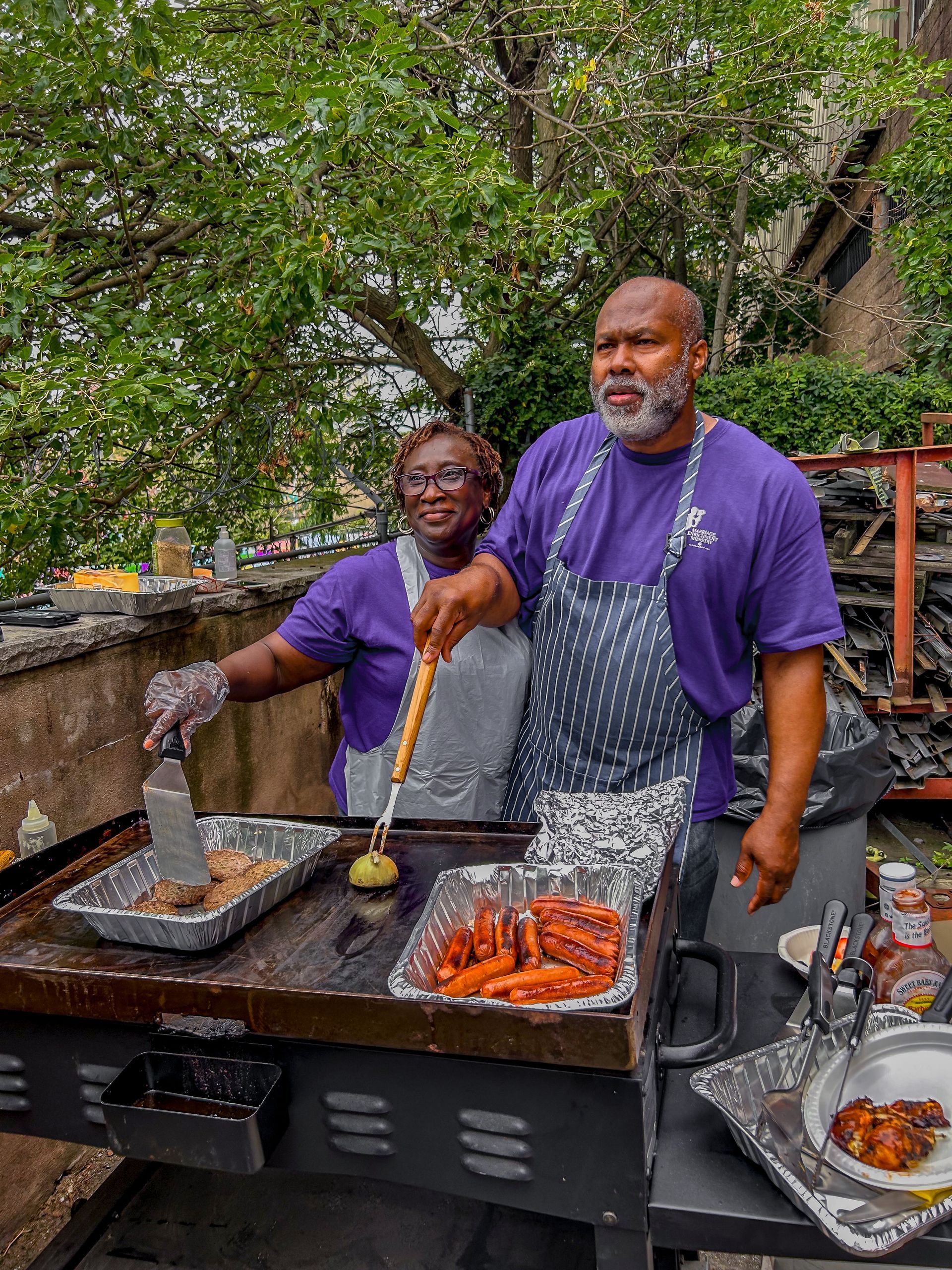A man and a woman are cooking food on a grill.