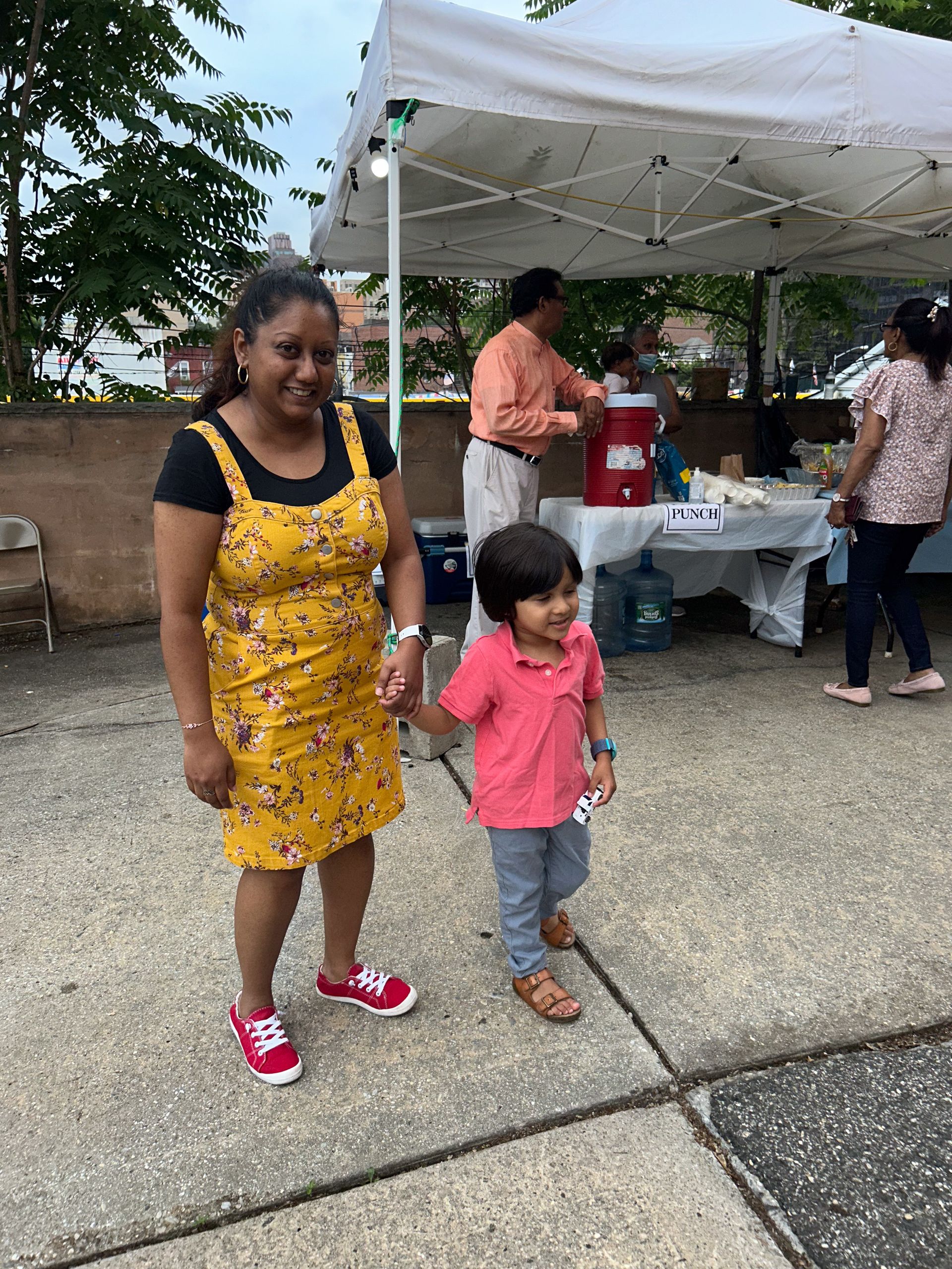 A woman and a child are standing on a sidewalk in front of a tent.