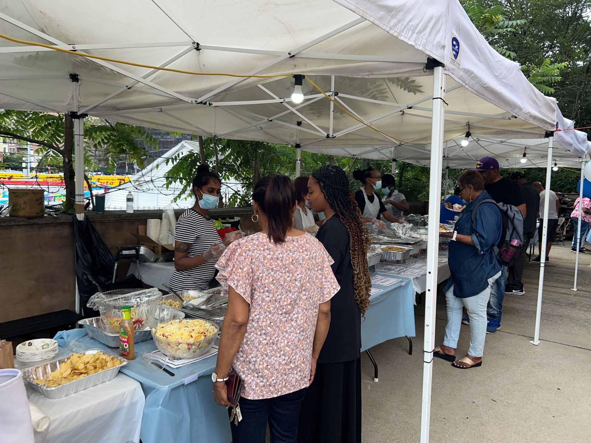 A group of people are standing under a tent eating food.