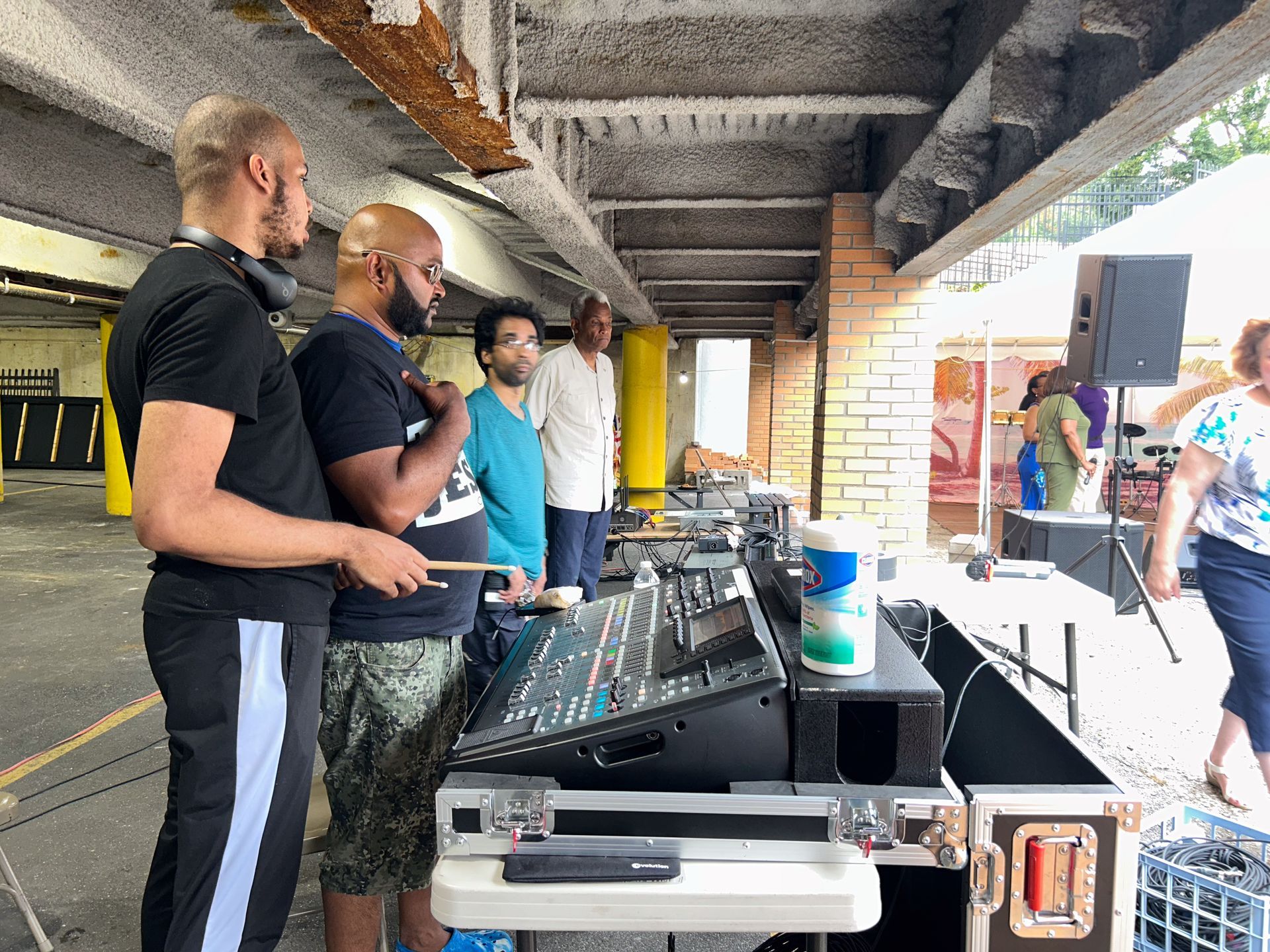 A group of men are standing around a dj booth in a parking garage.