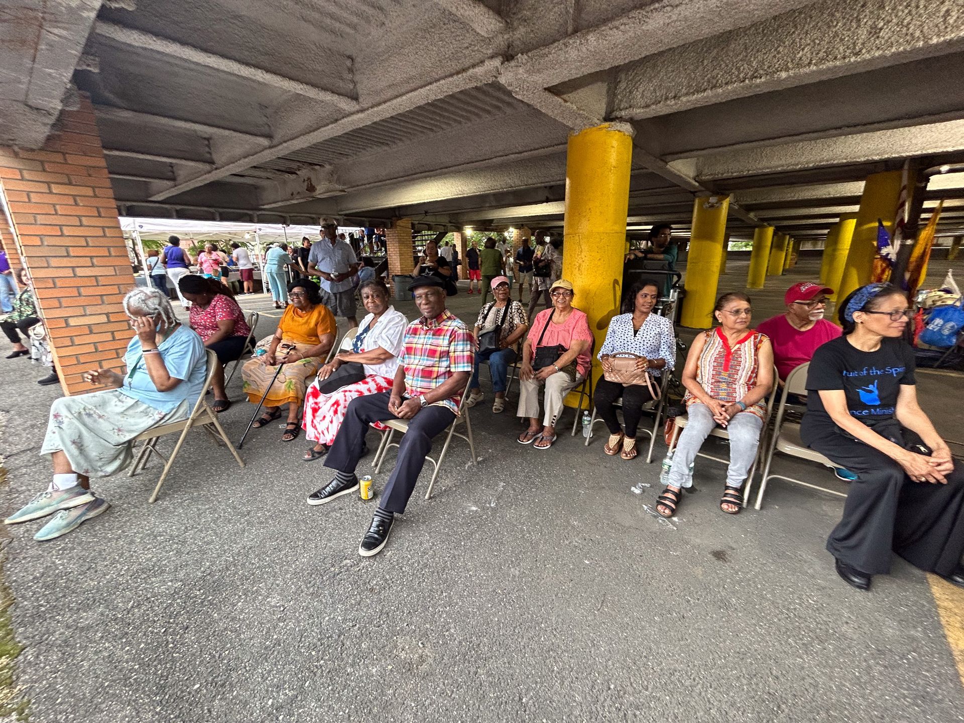 A group of people are sitting in chairs under a bridge.