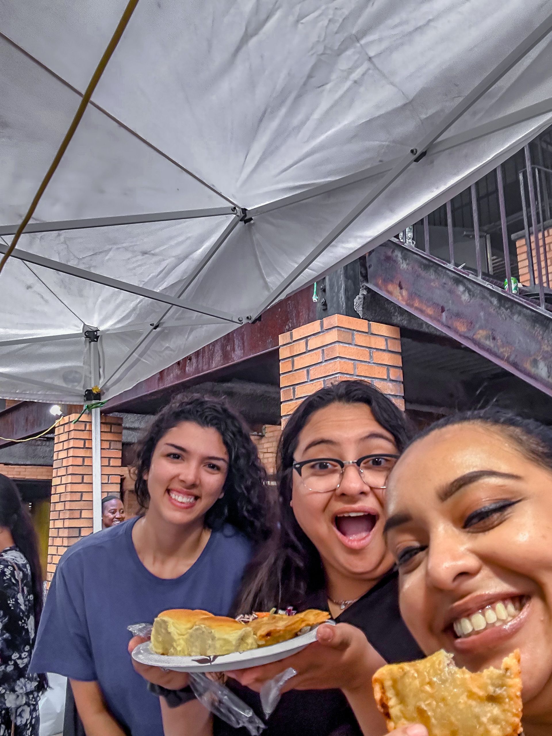 Three women are posing for a picture while holding plates of food.