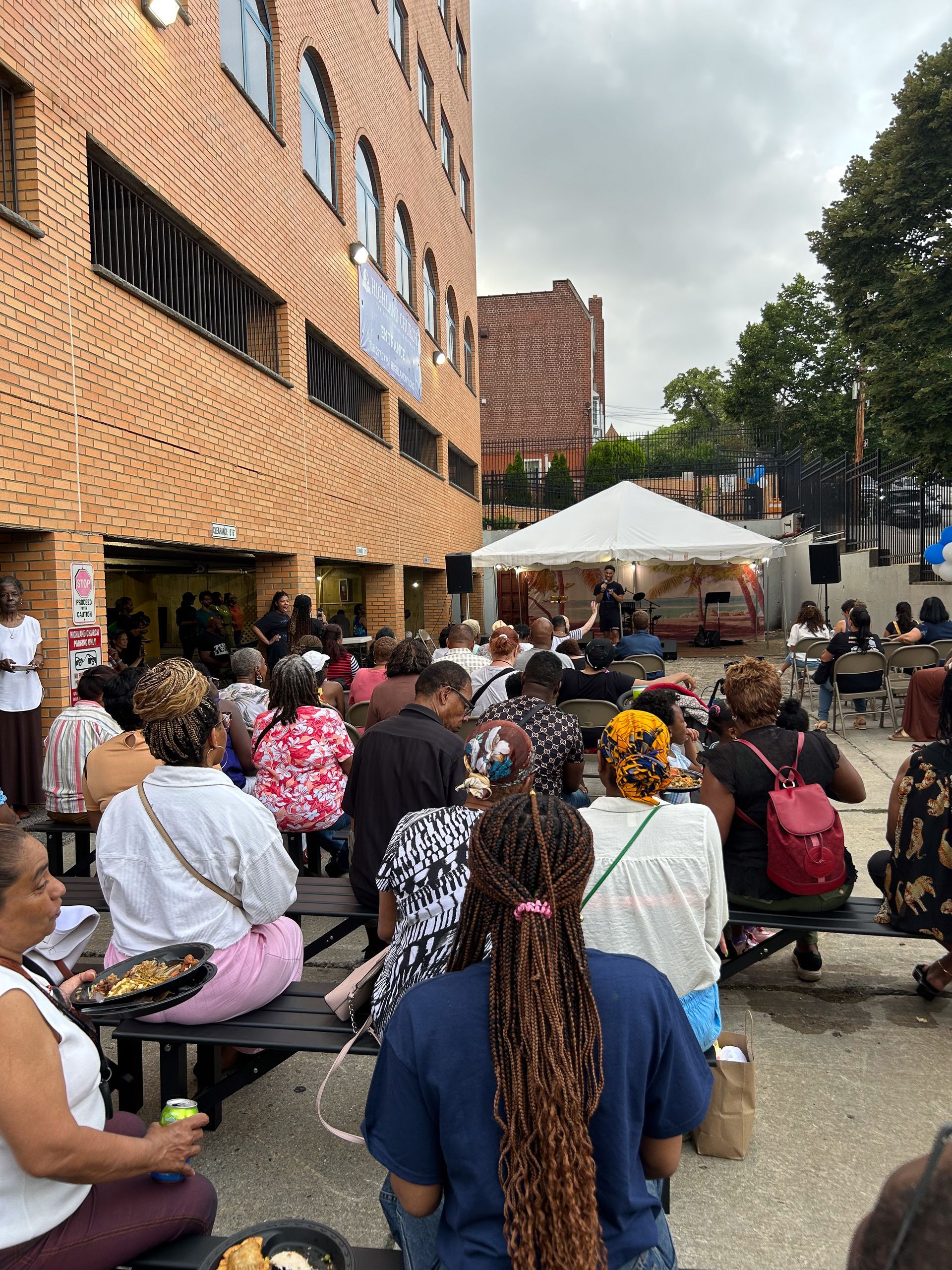 A large group of people are sitting at picnic tables outside of a building.