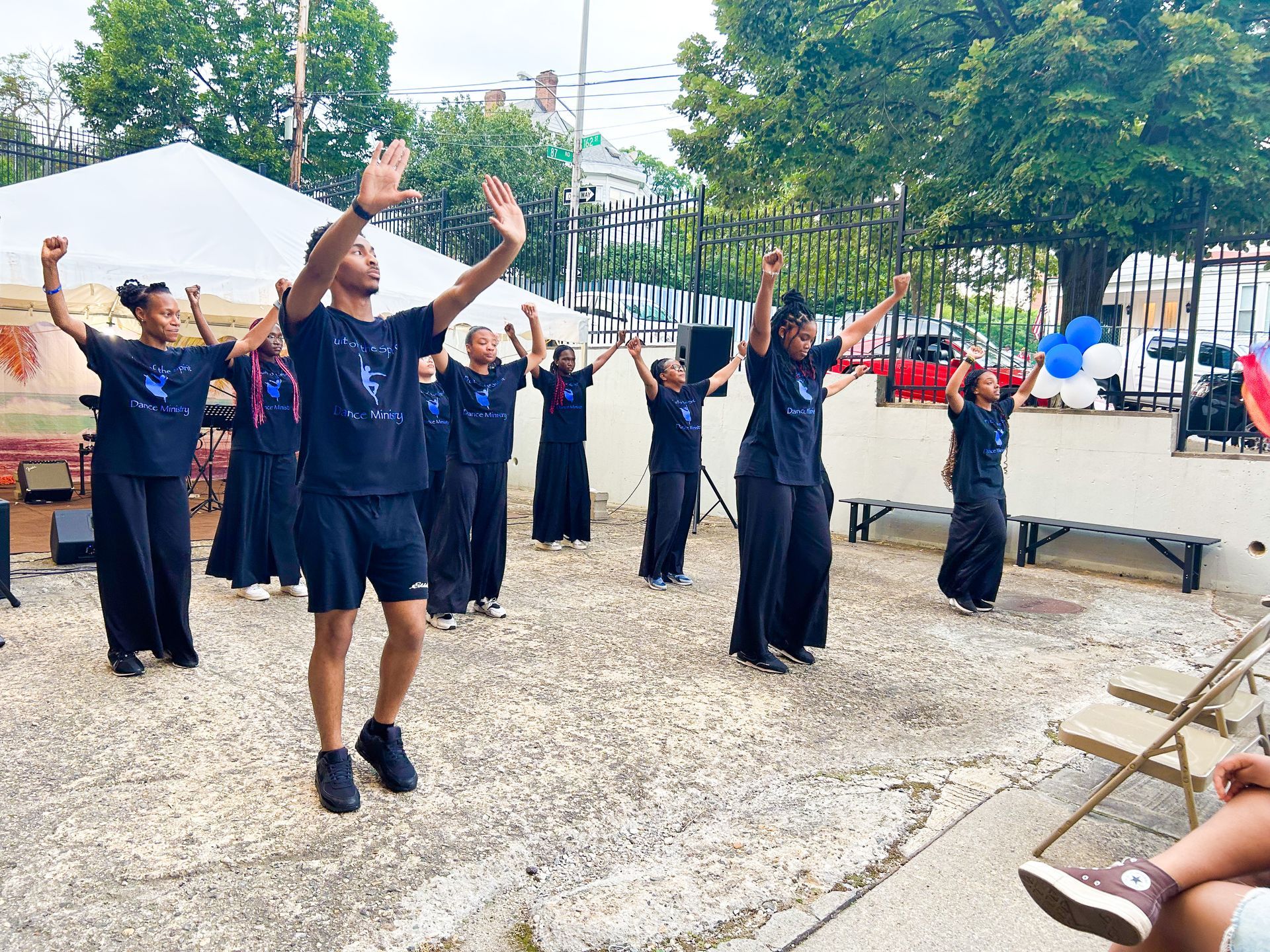 A group of people are dancing in a park with their arms in the air.