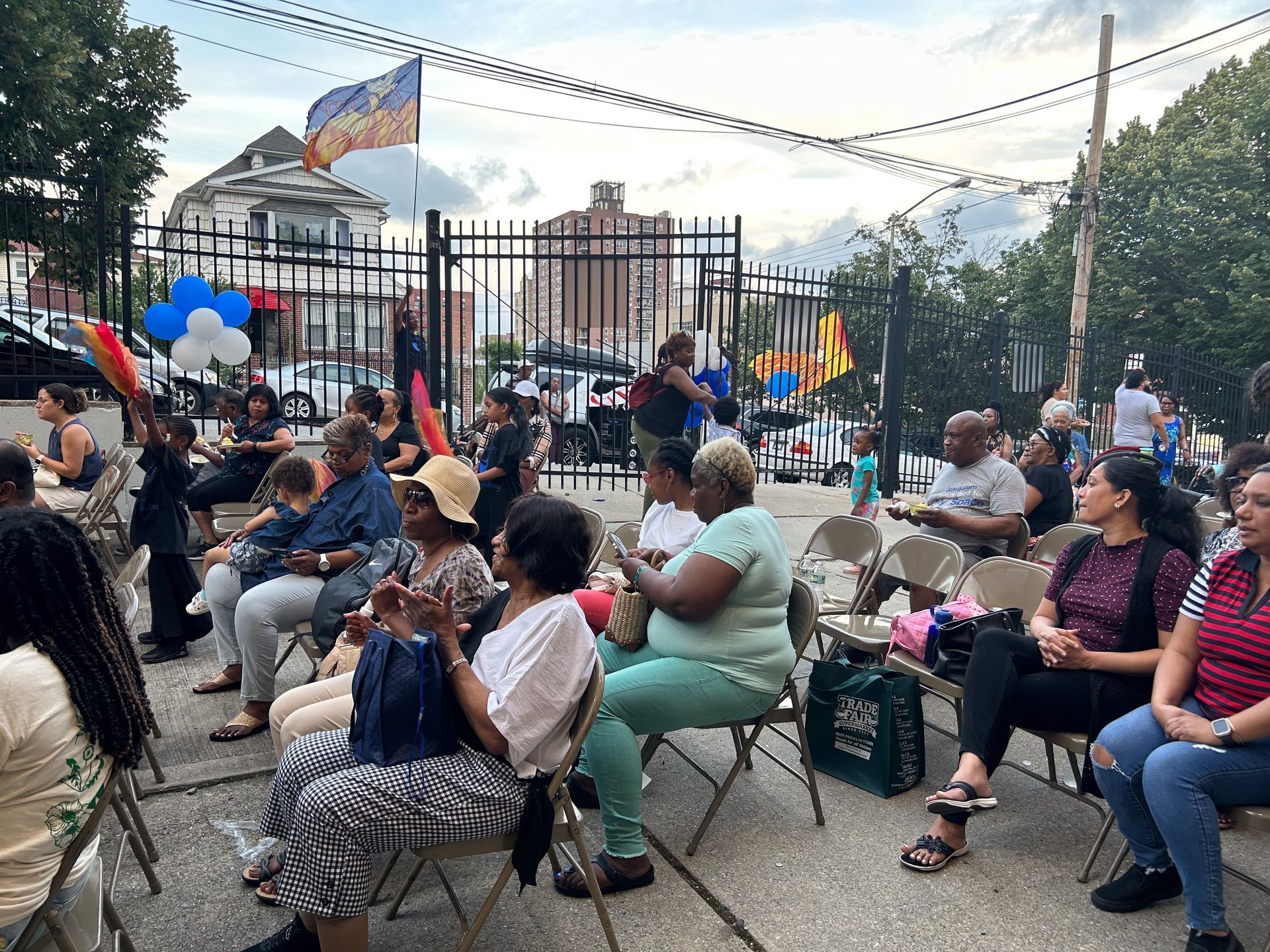 A group of people are sitting in folding chairs in front of a fence.