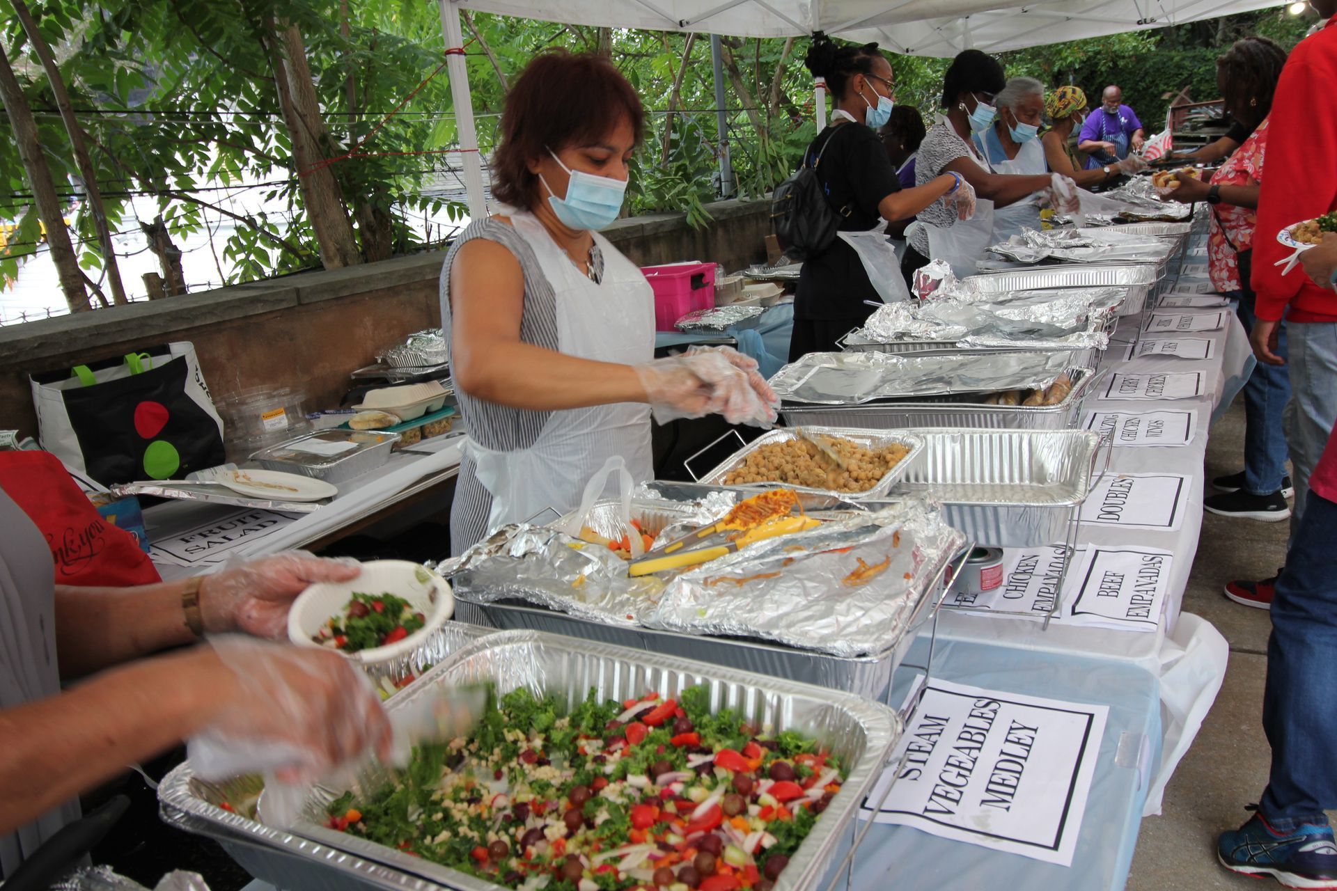 A woman wearing a mask is serving food at a buffet table.