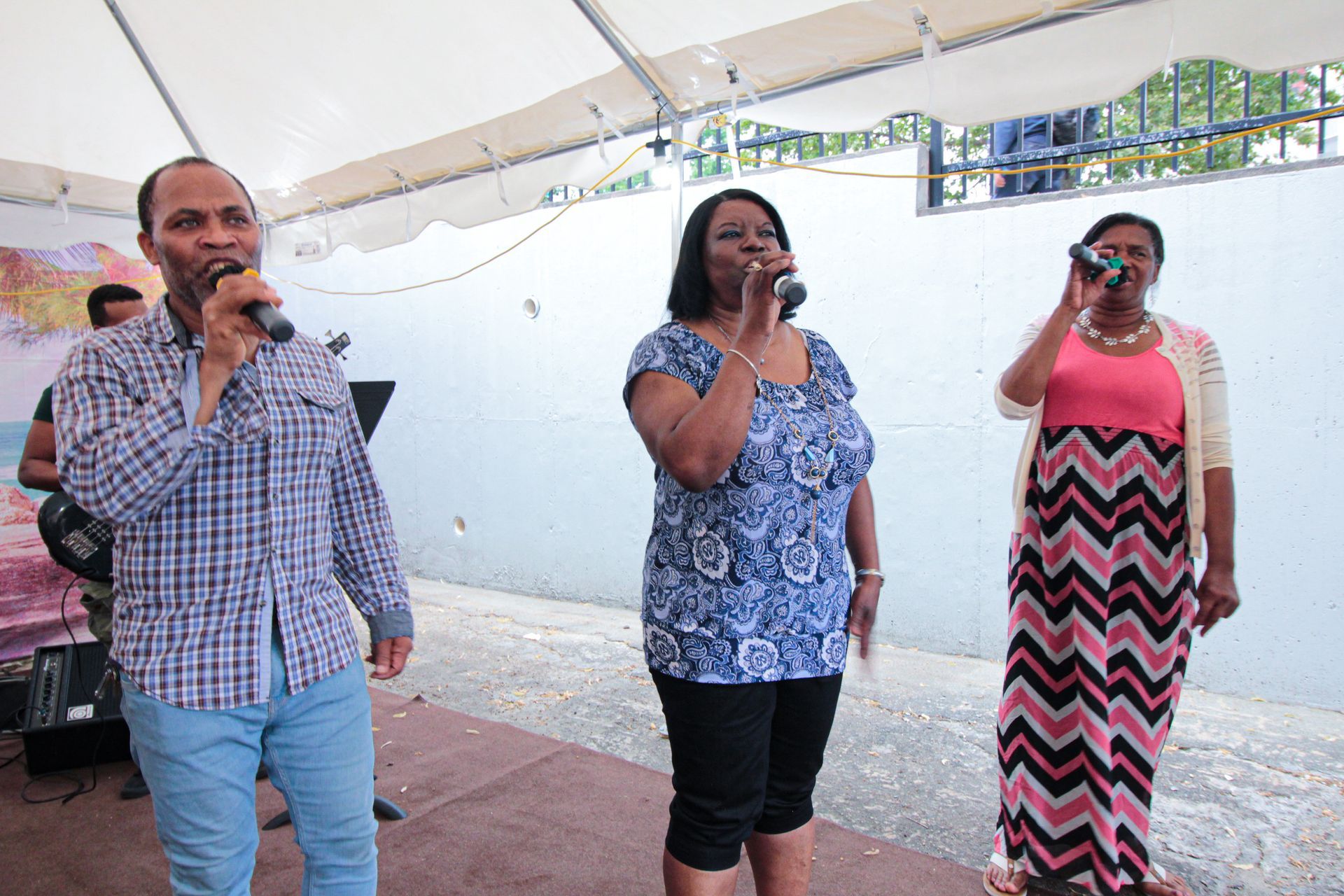 A man and two women singing into microphones under a tent