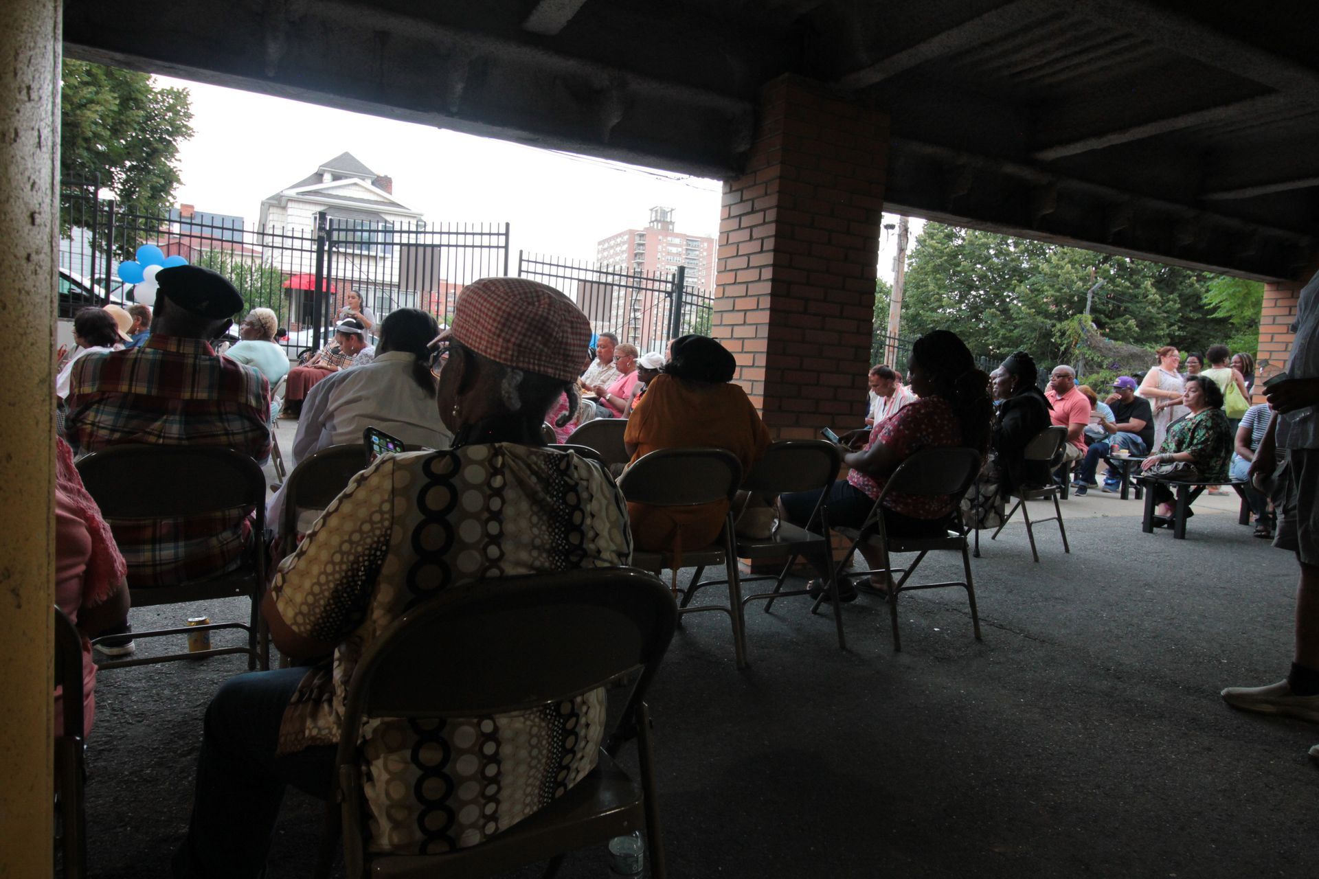 A group of people are sitting in chairs under a covered area.