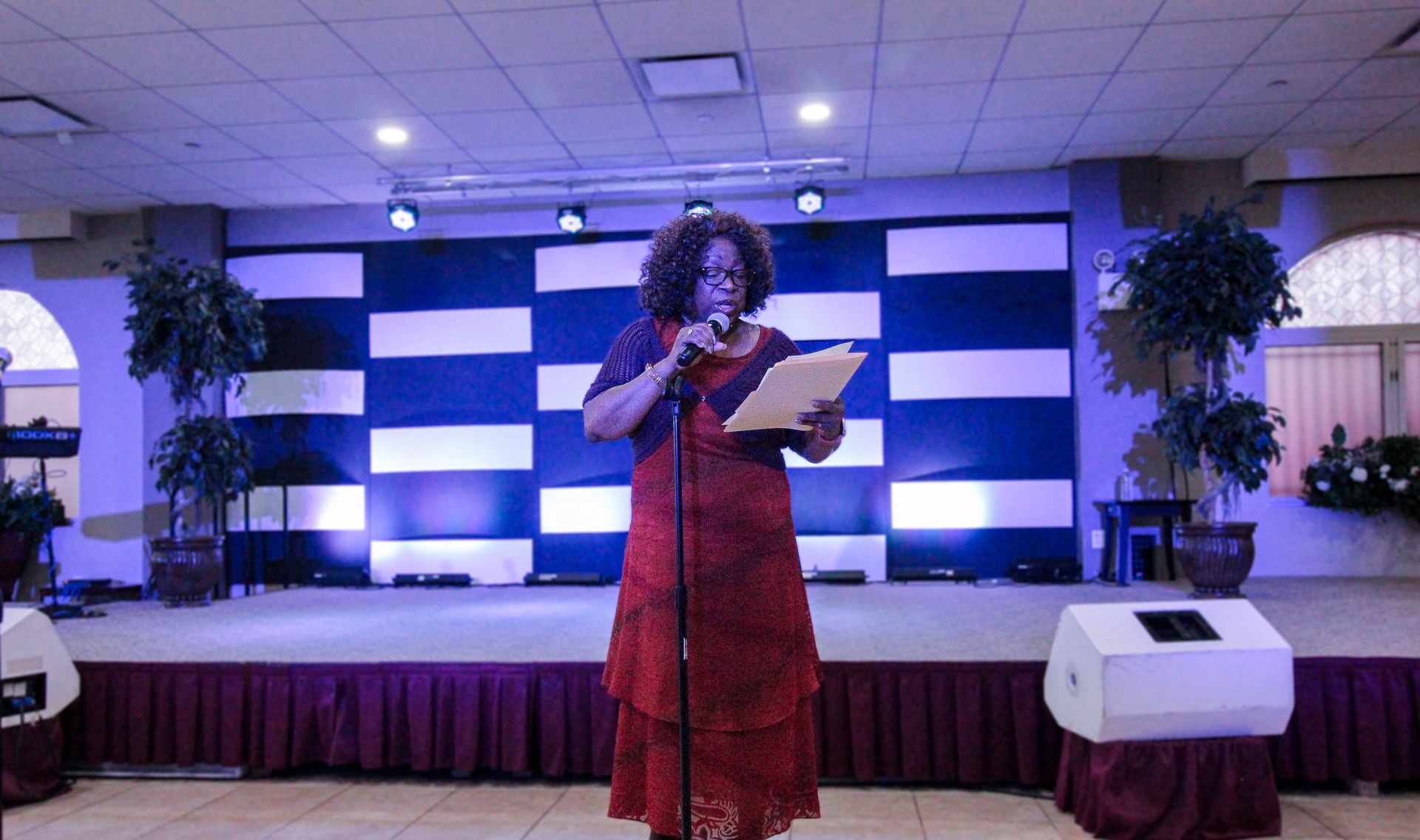 A woman in a red dress is standing on a stage holding a piece of paper in front of a microphone.