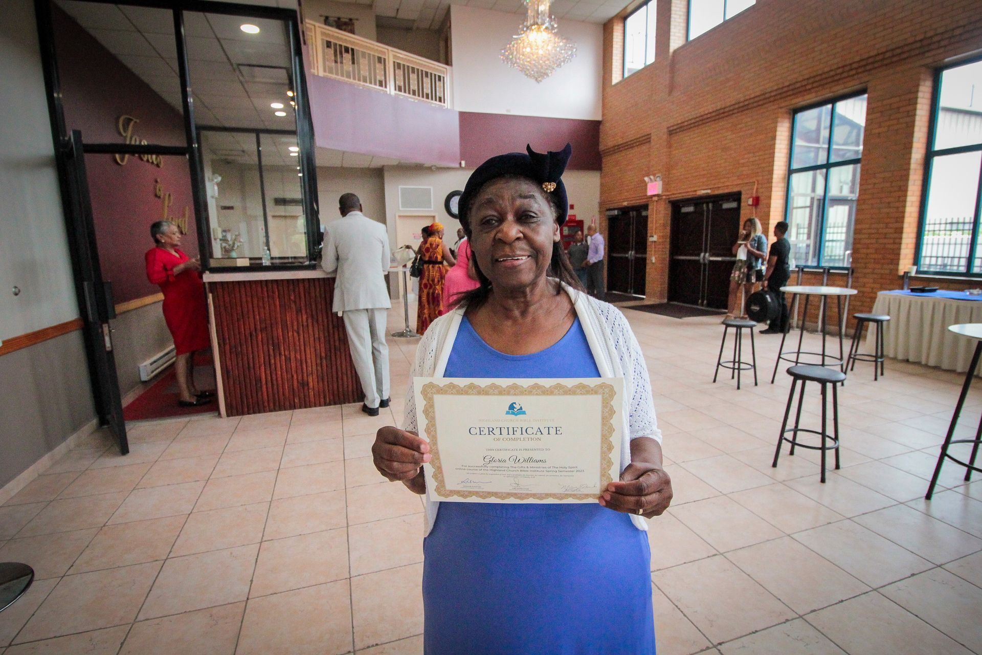 A woman in a blue dress is holding a certificate in a room.