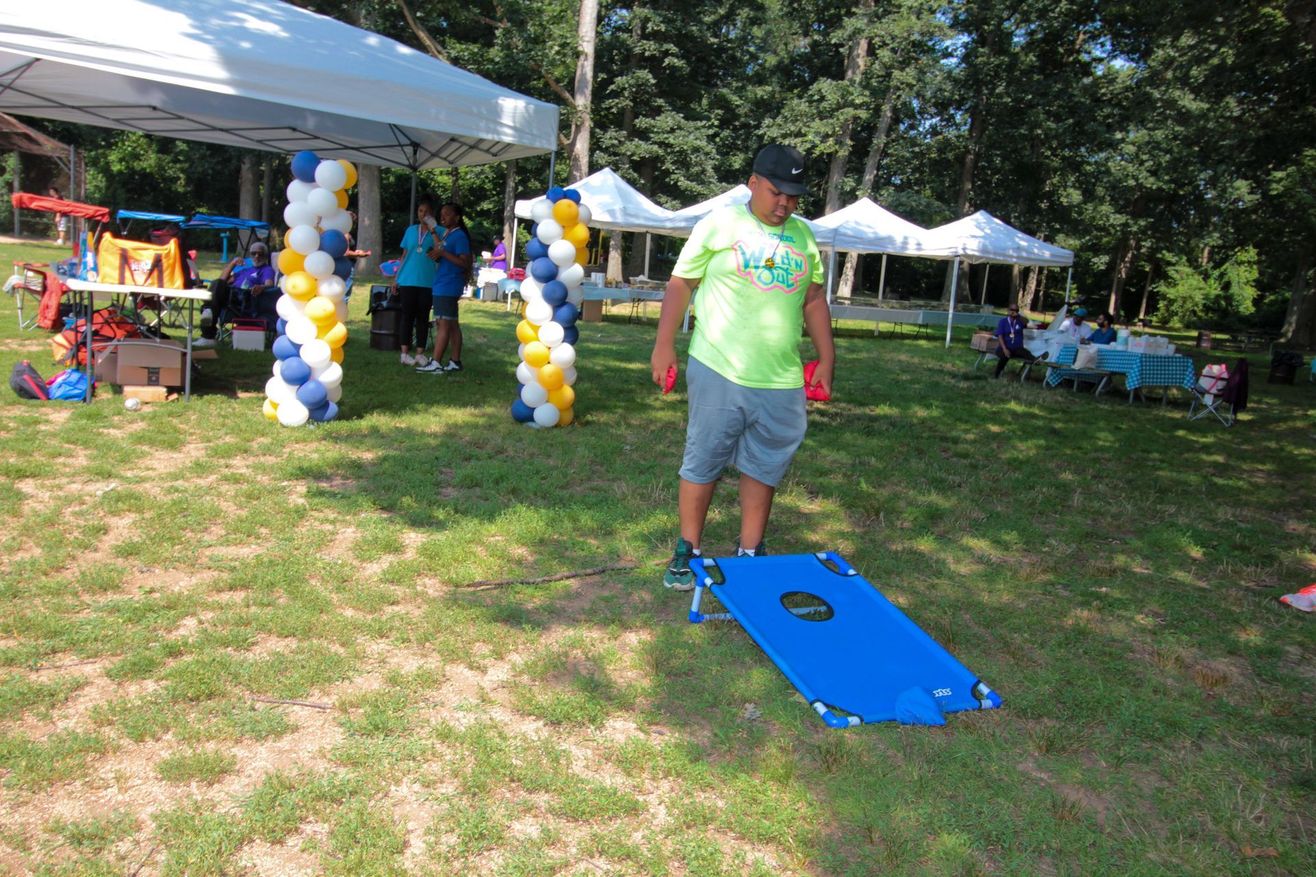 A man in a green shirt is playing cornhole in a park.