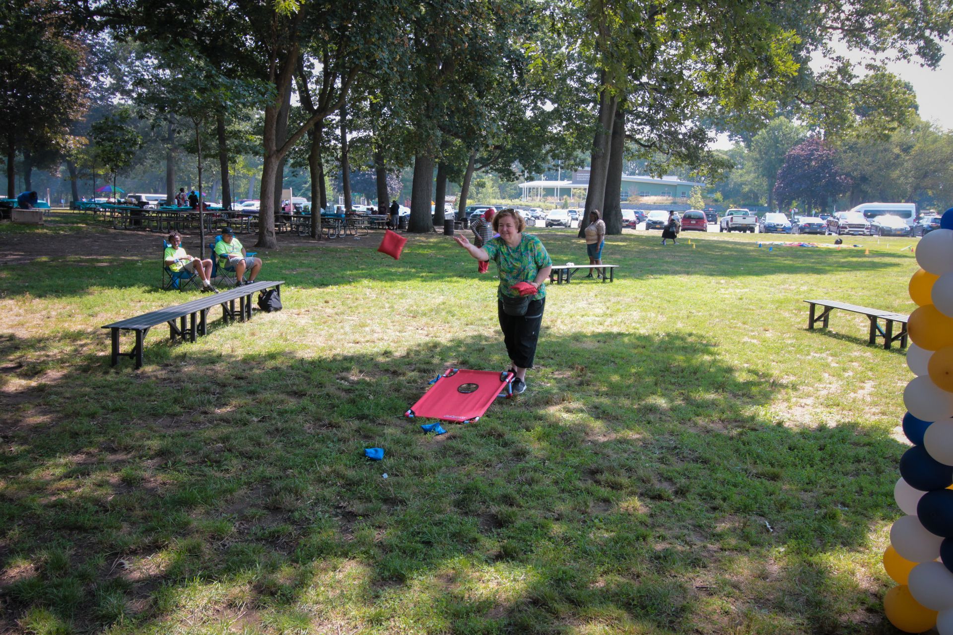 A woman is playing a game of cornhole in a park.
