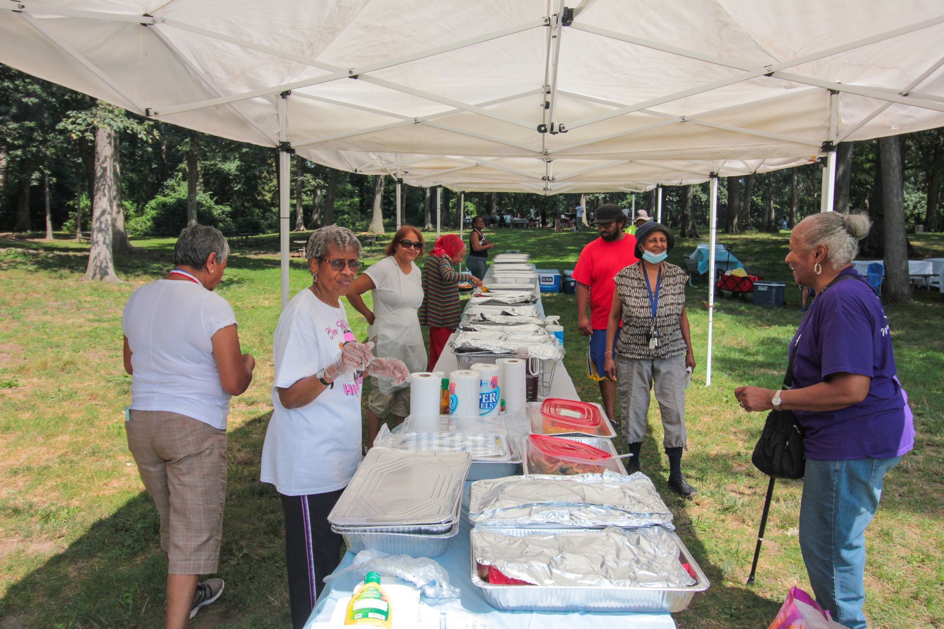 A group of people are standing around a long table under a tent.