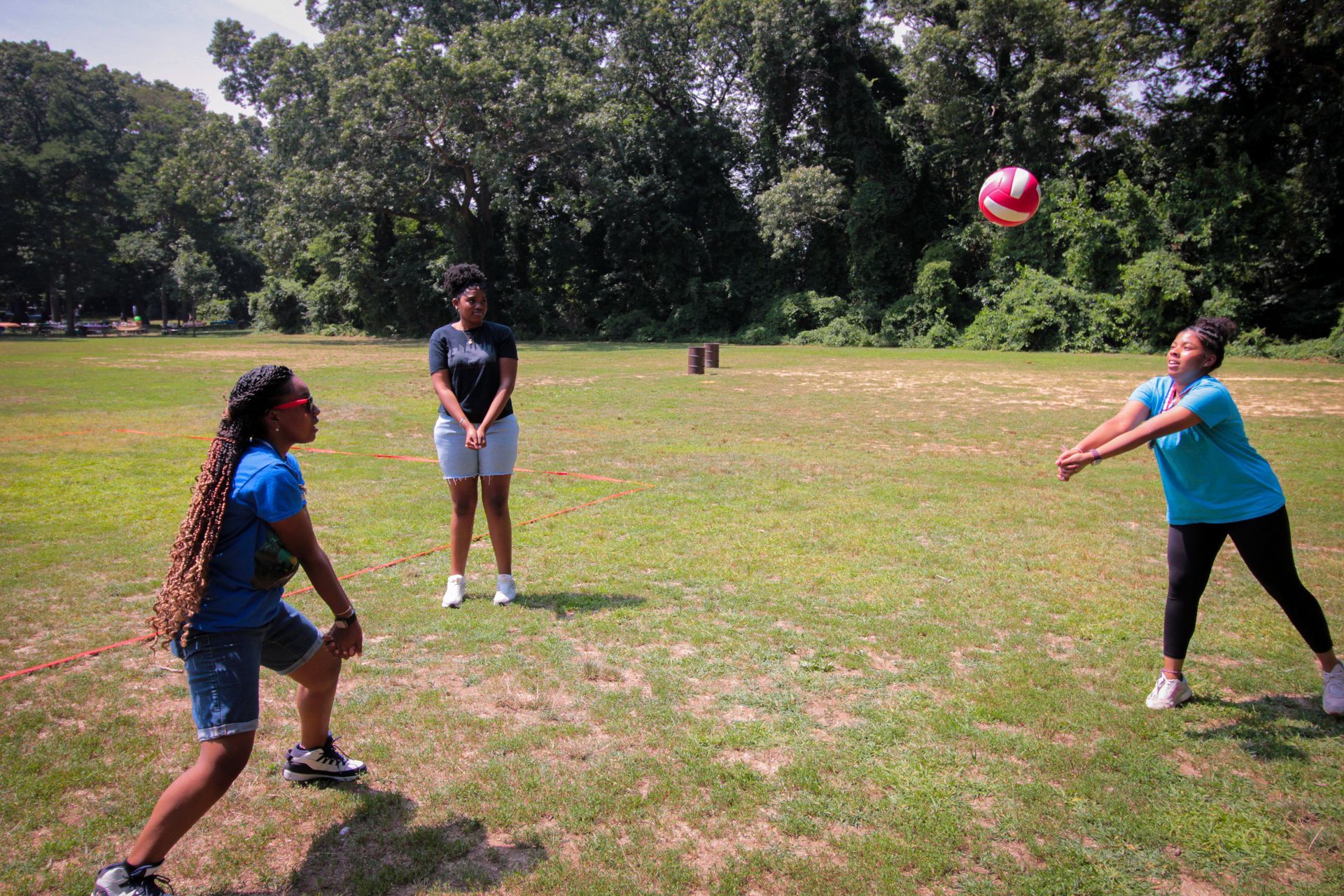 Three women are playing volleyball in a field.