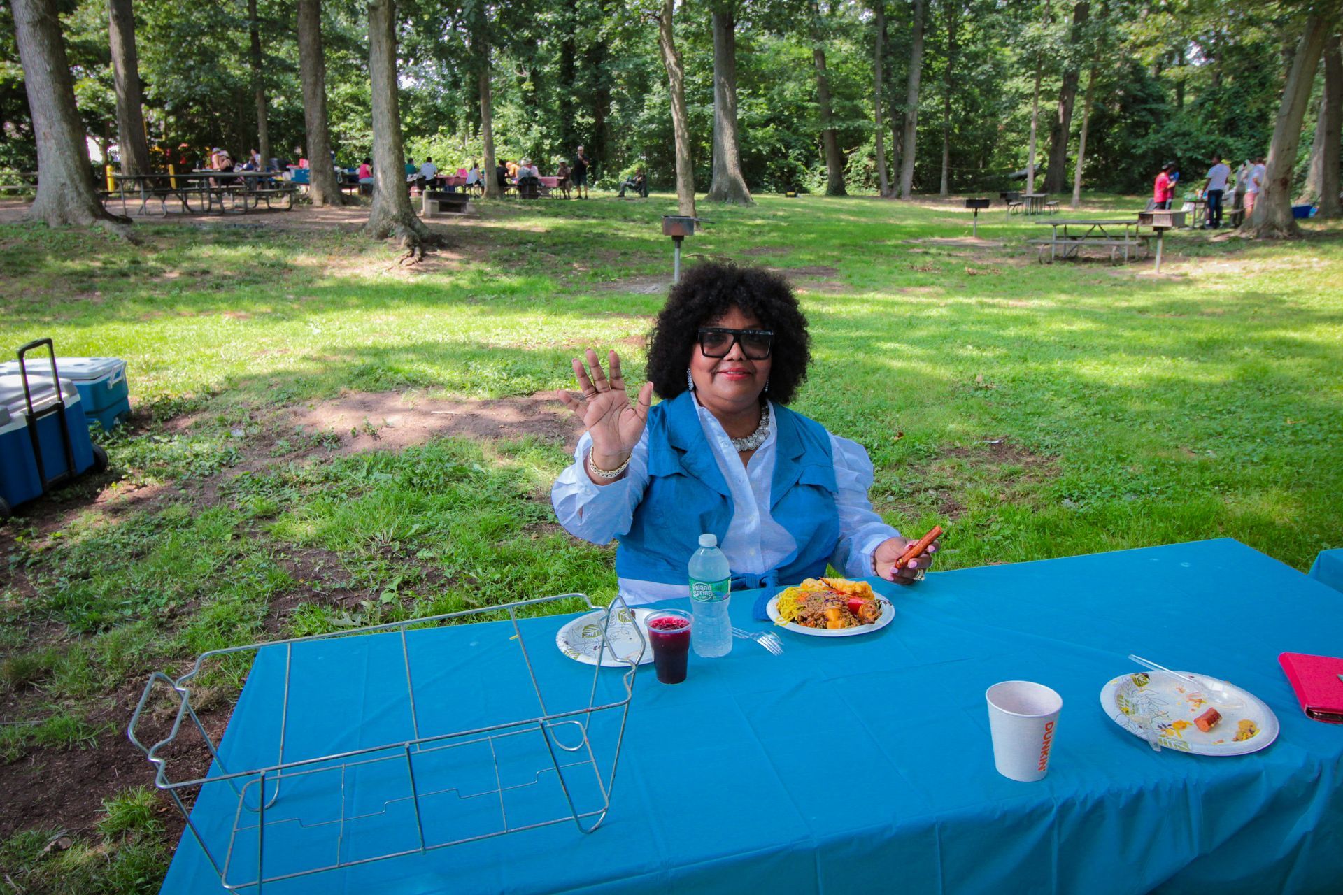 A woman is sitting at a table in a park eating food.
