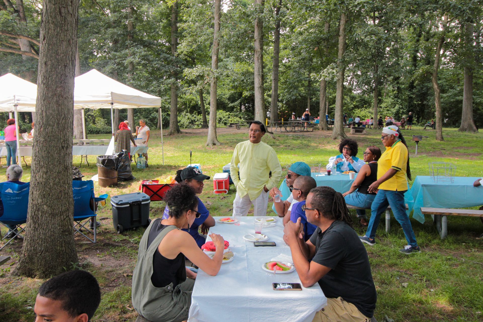A group of people are sitting at a table in a park.