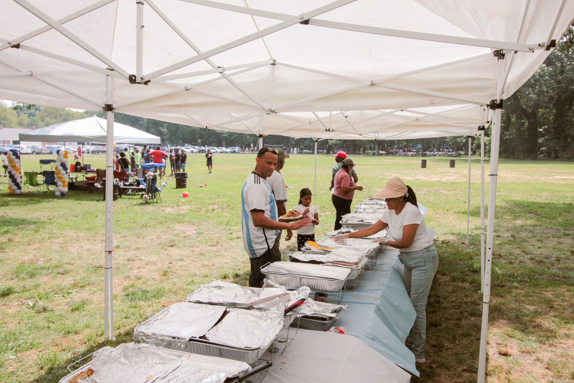 A group of people are standing around a table under a tent in a field.