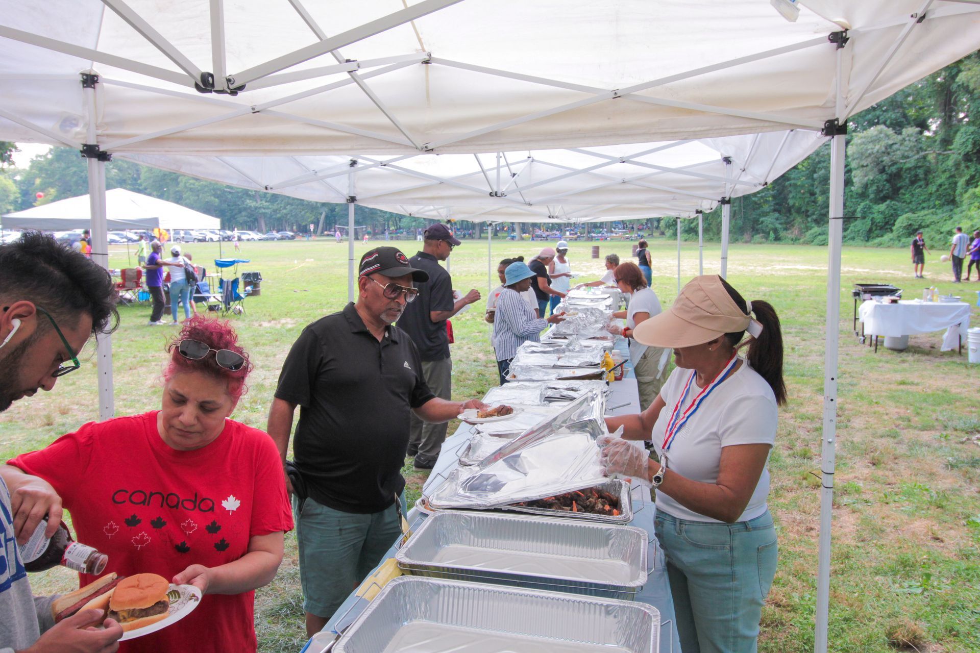 A group of people are standing under a tent eating food.