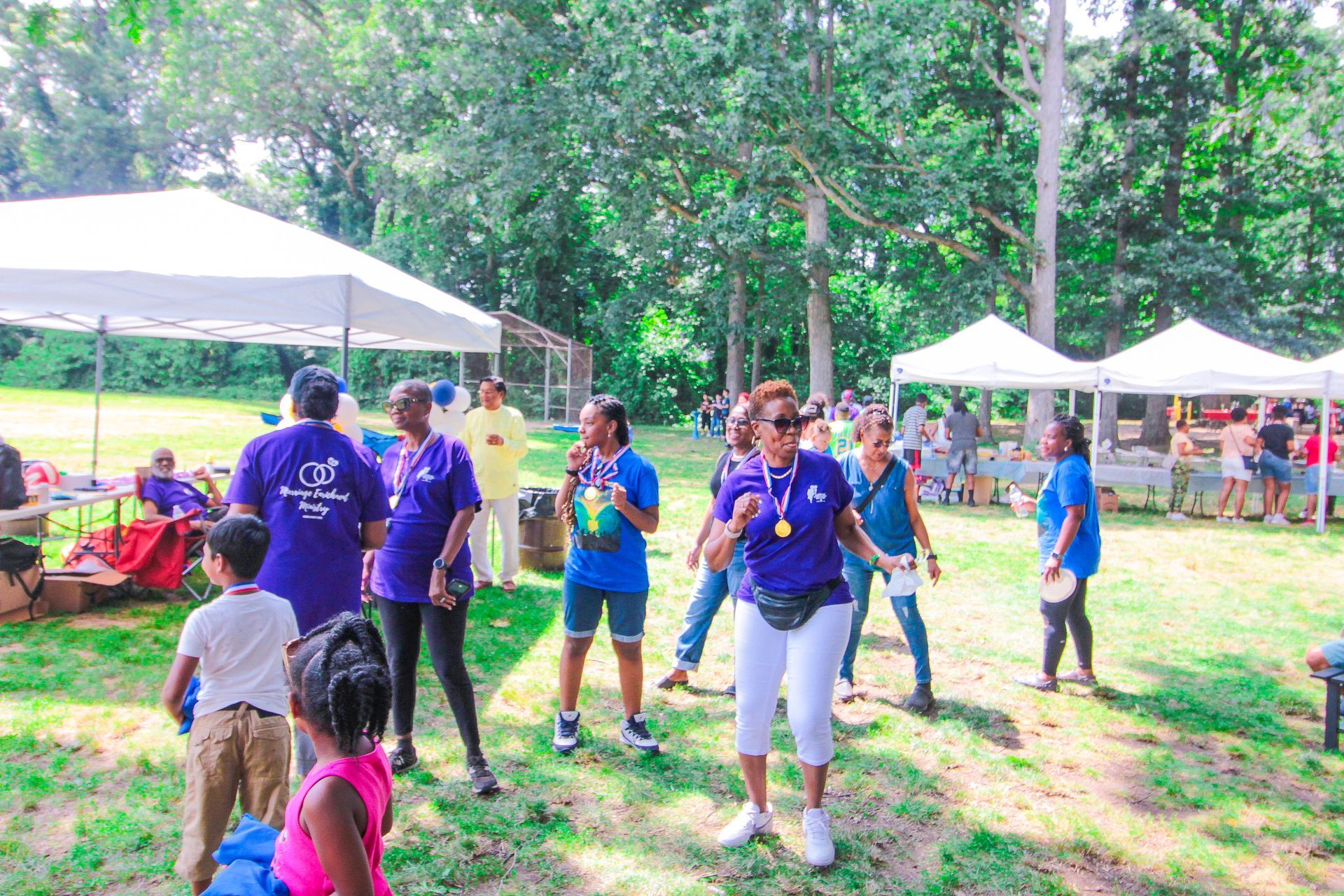 A group of people are standing in a park under tents.