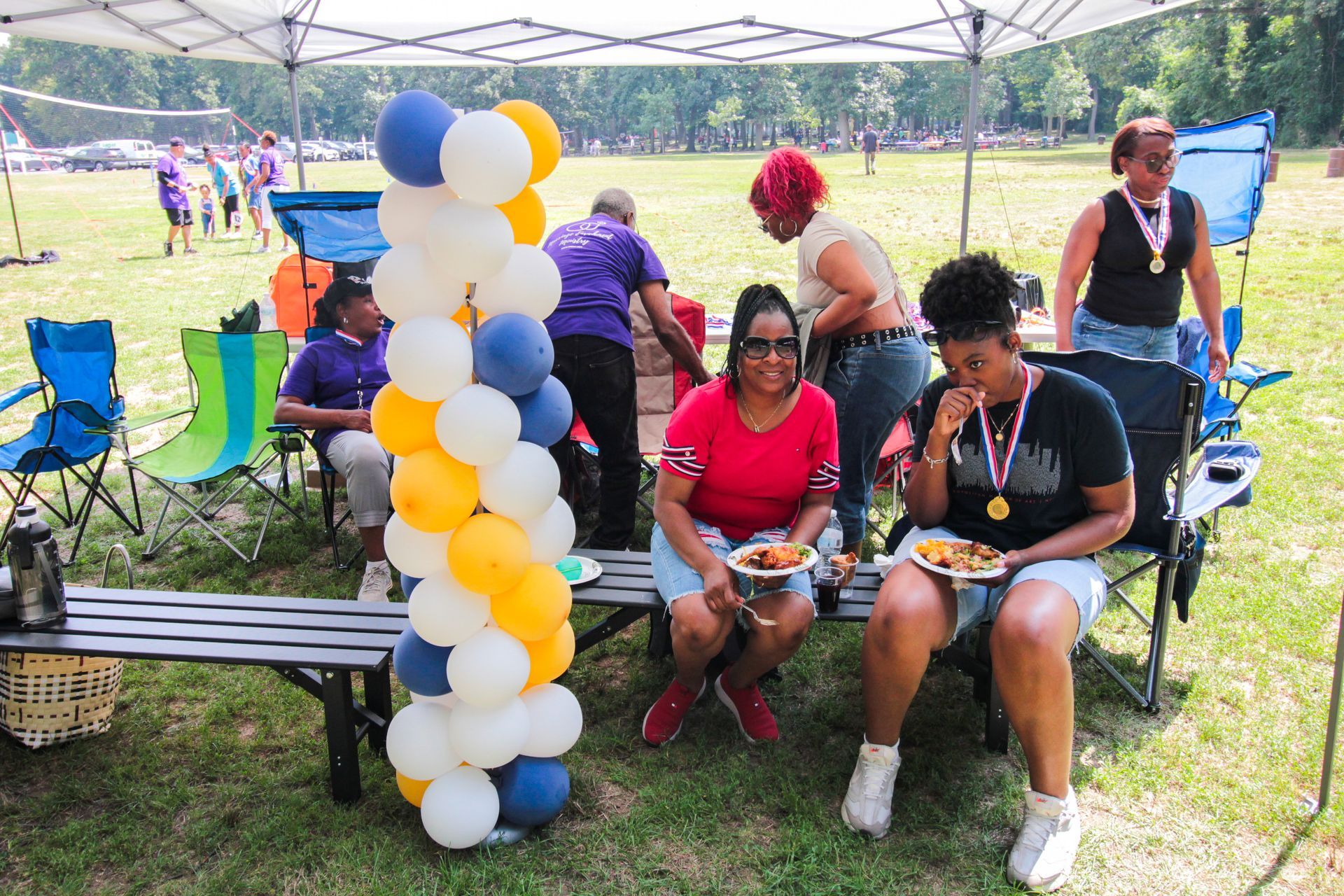 A group of people are sitting on benches under a tent eating food.