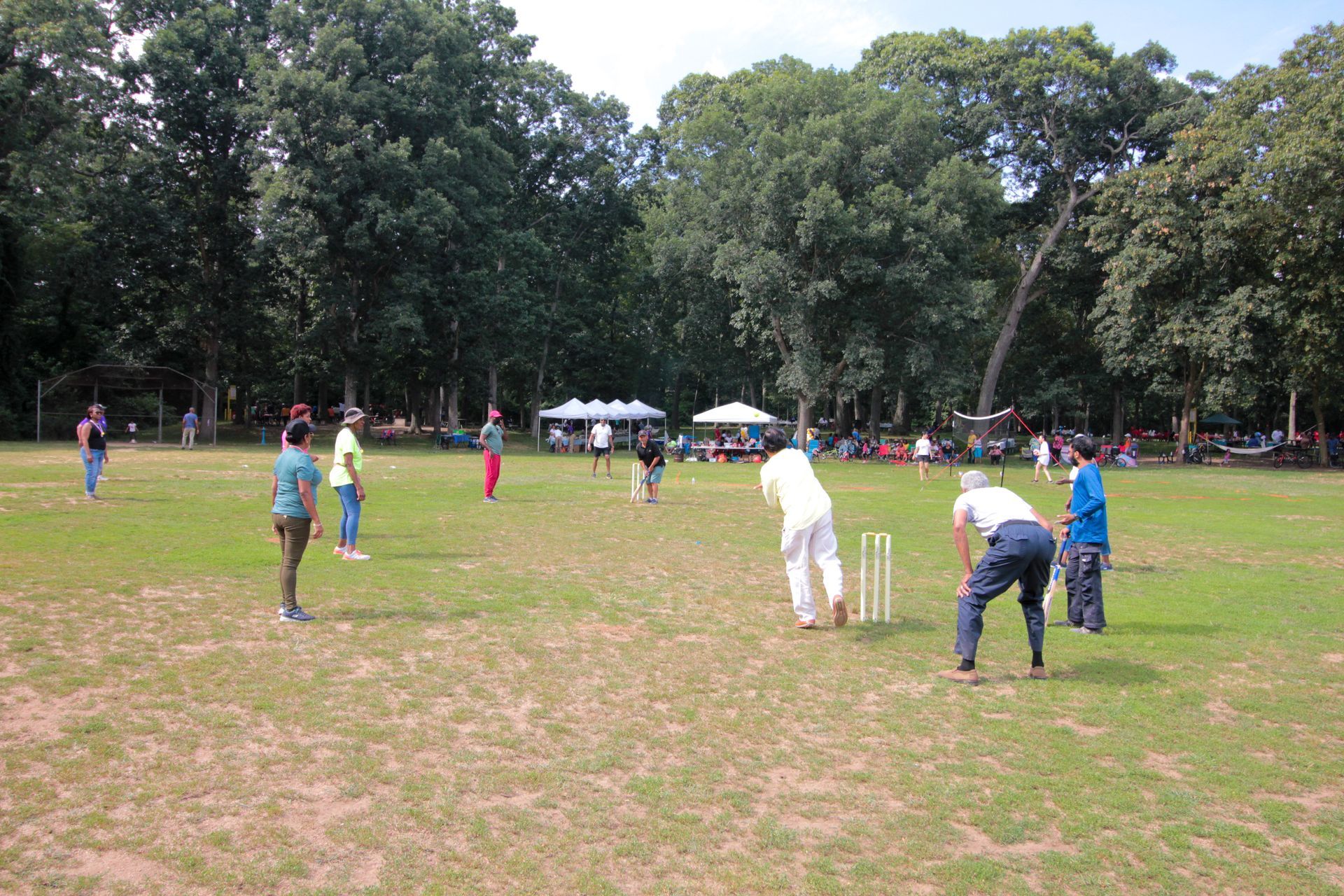 A group of people are playing a game of cricket in a field.