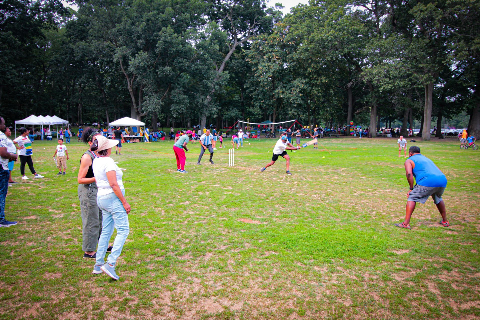 A group of people are playing a game of cricket in a park.