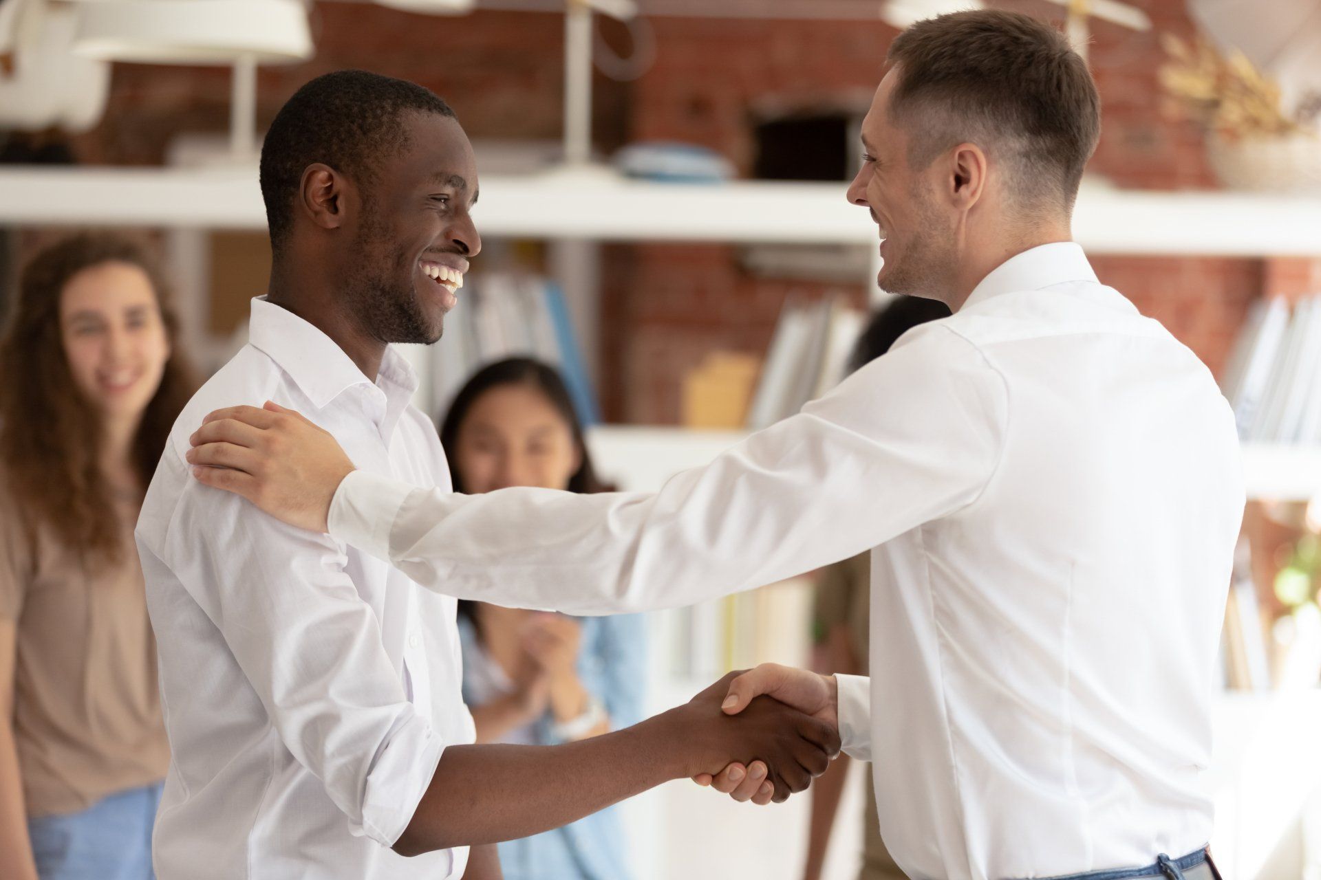 Two men are shaking hands in front of a group of people.