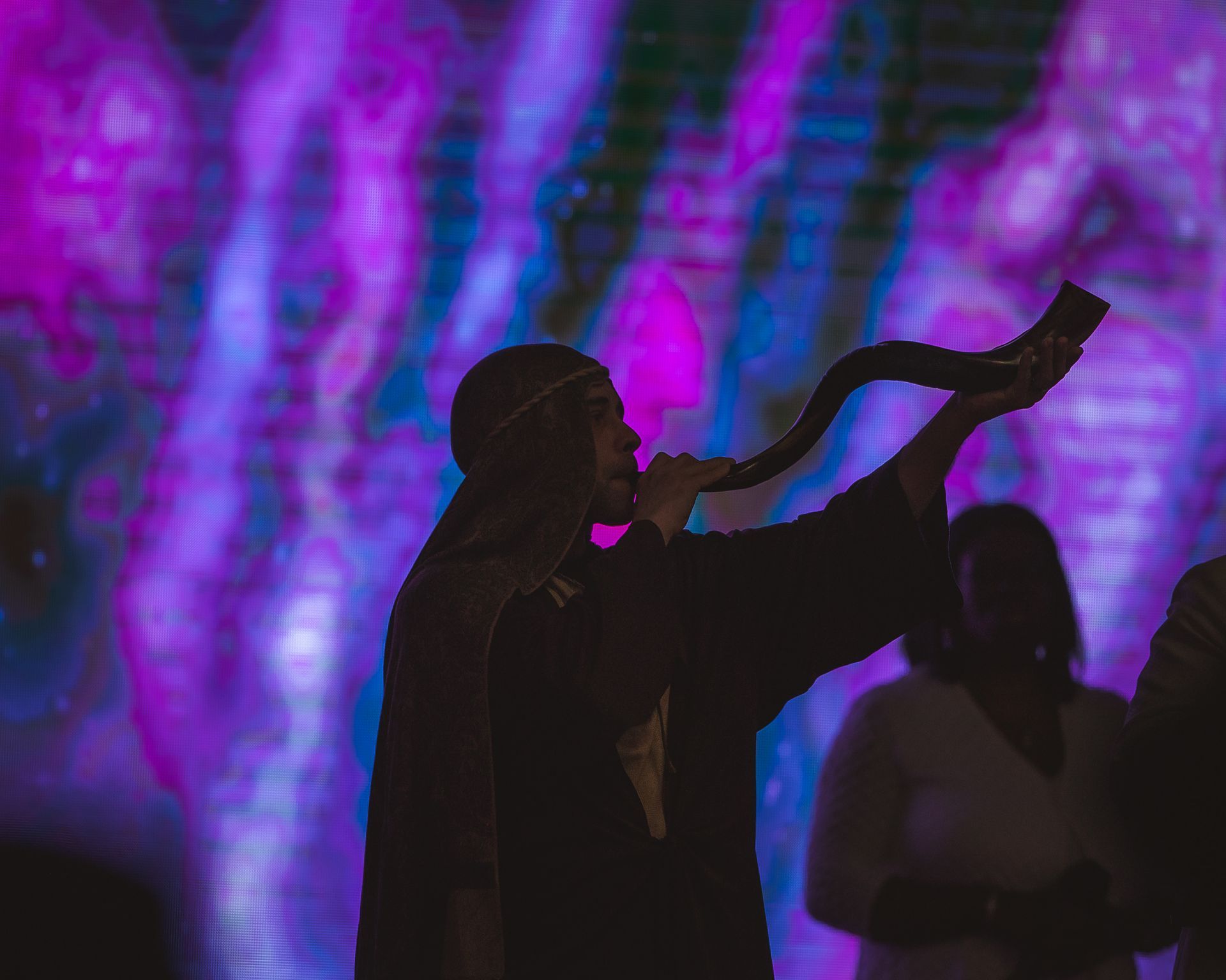 A man is blowing a horn in front of a colorful background.