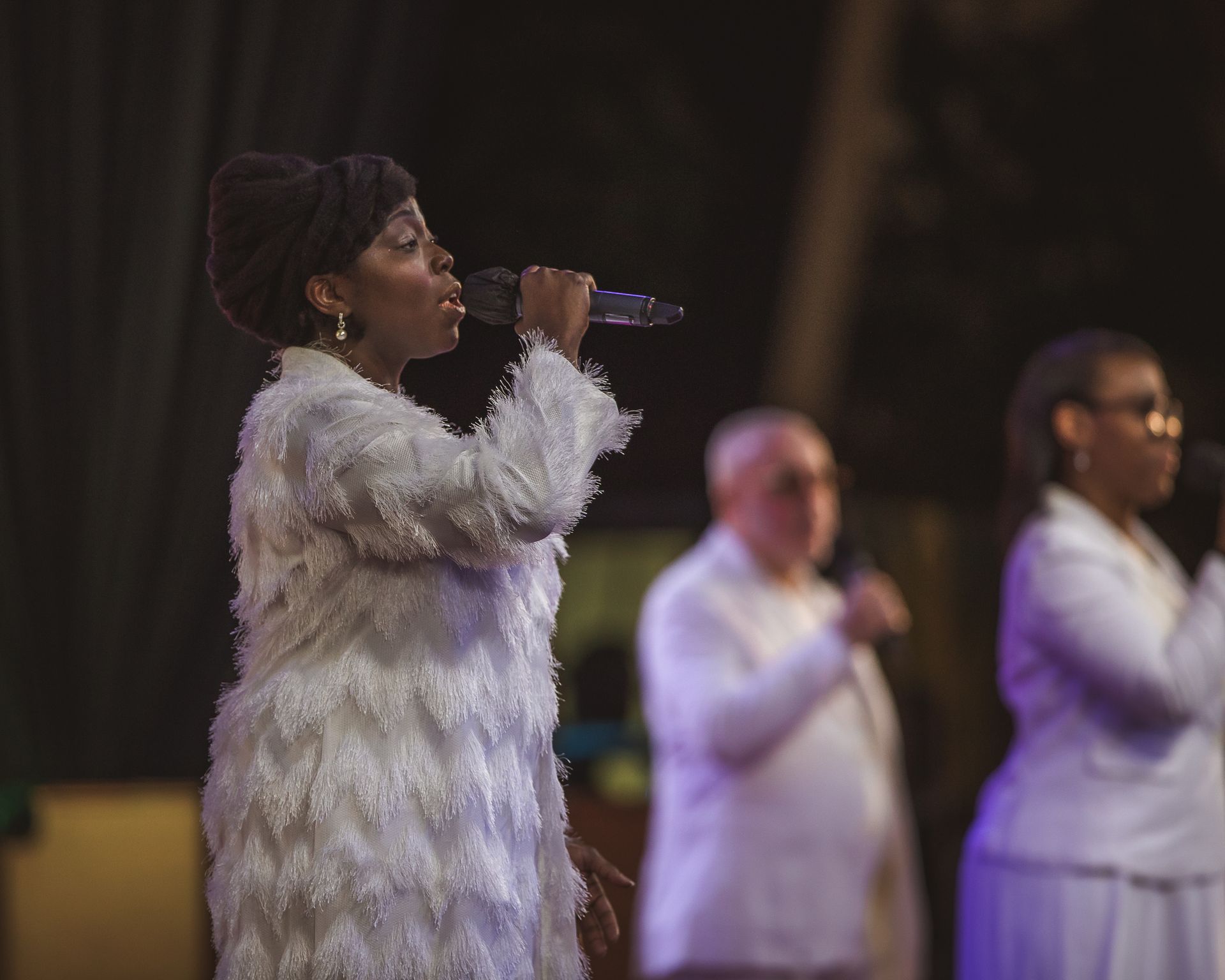 A woman in a white fur coat is singing into a microphone.